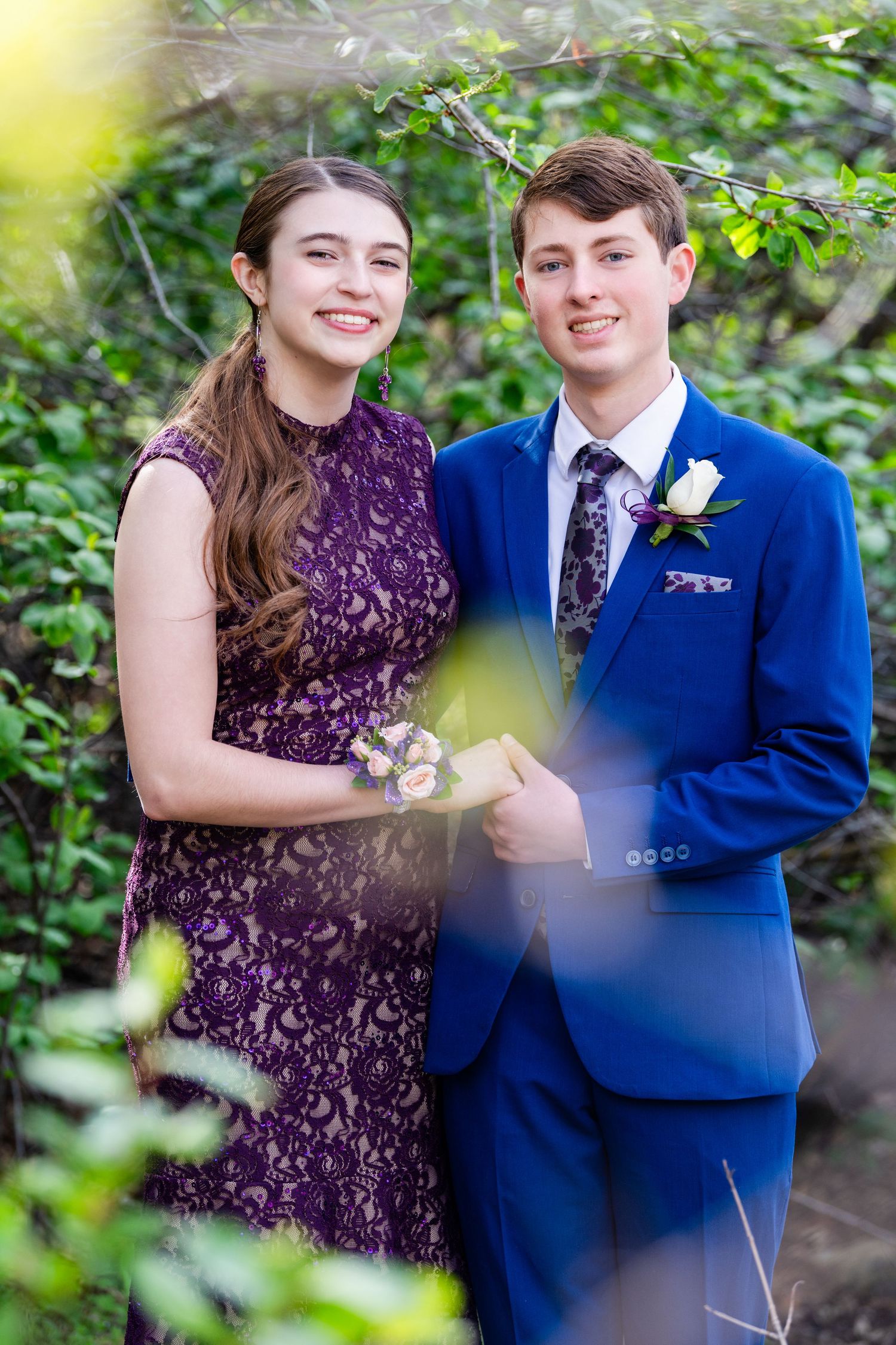 Prom couple portrait framed by greenery with purple dress and blue suit
