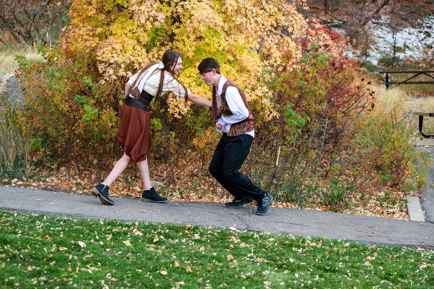 Couple playfully facing off on path in pirate themed outfits with fall foliage background for Sadie Hawkins dance