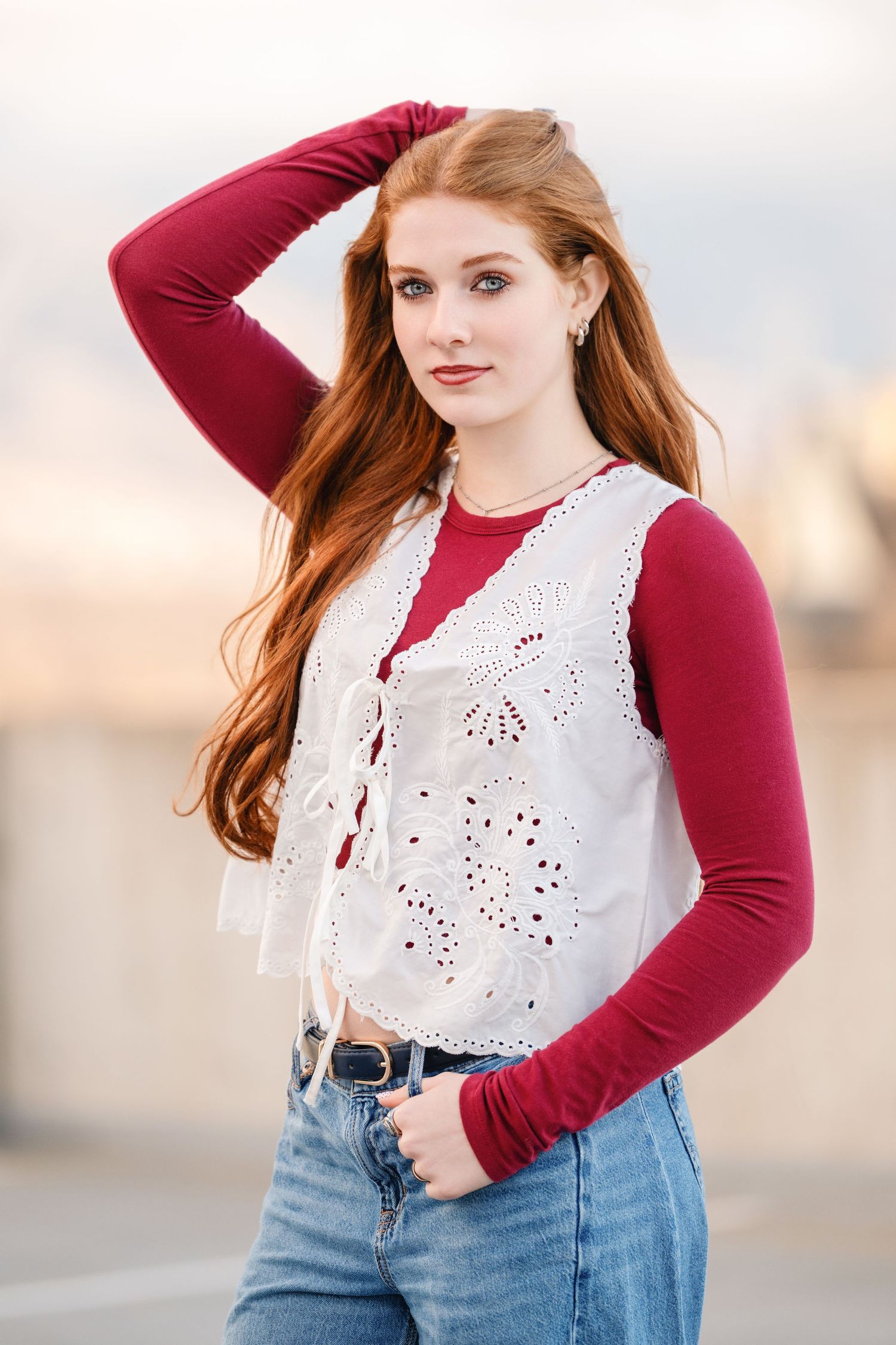 Senior girl portrait with hand in hair wearing layered outfit in soft golden light with confident pose