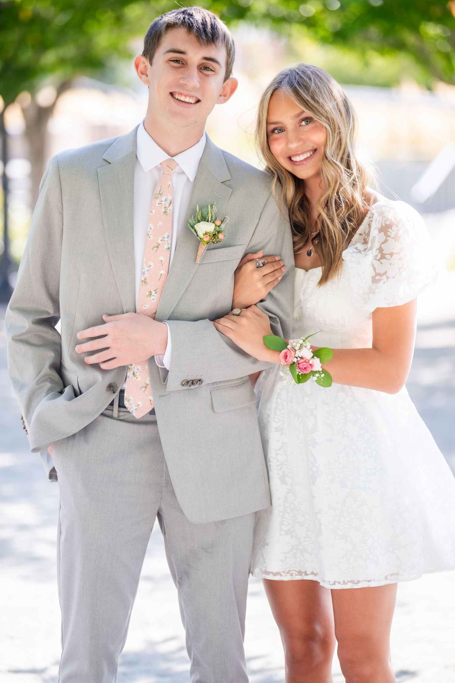Teen couple smiling together in light outfits with soft outdoor background