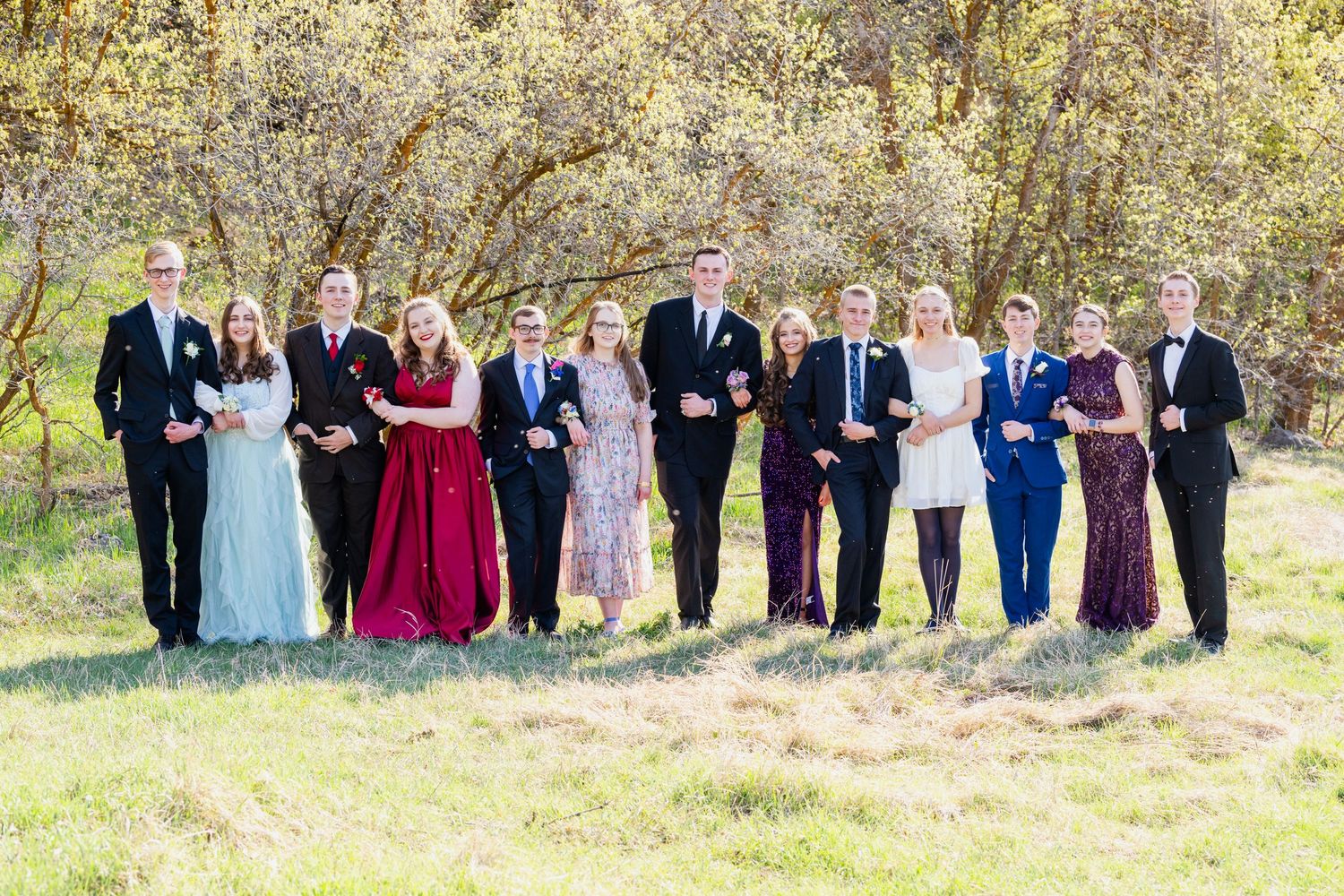 Large prom group lined up outdoors in formal attire with natural background