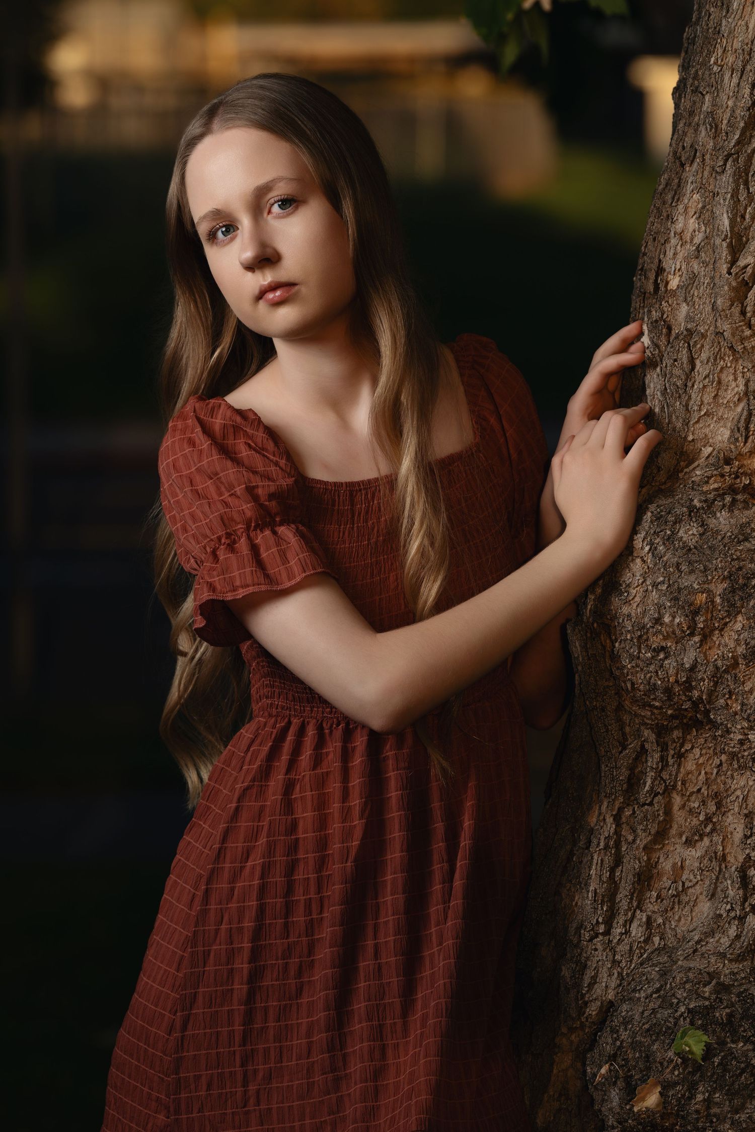 Young girl in red dress leaning against tree in soft studio light with moody background