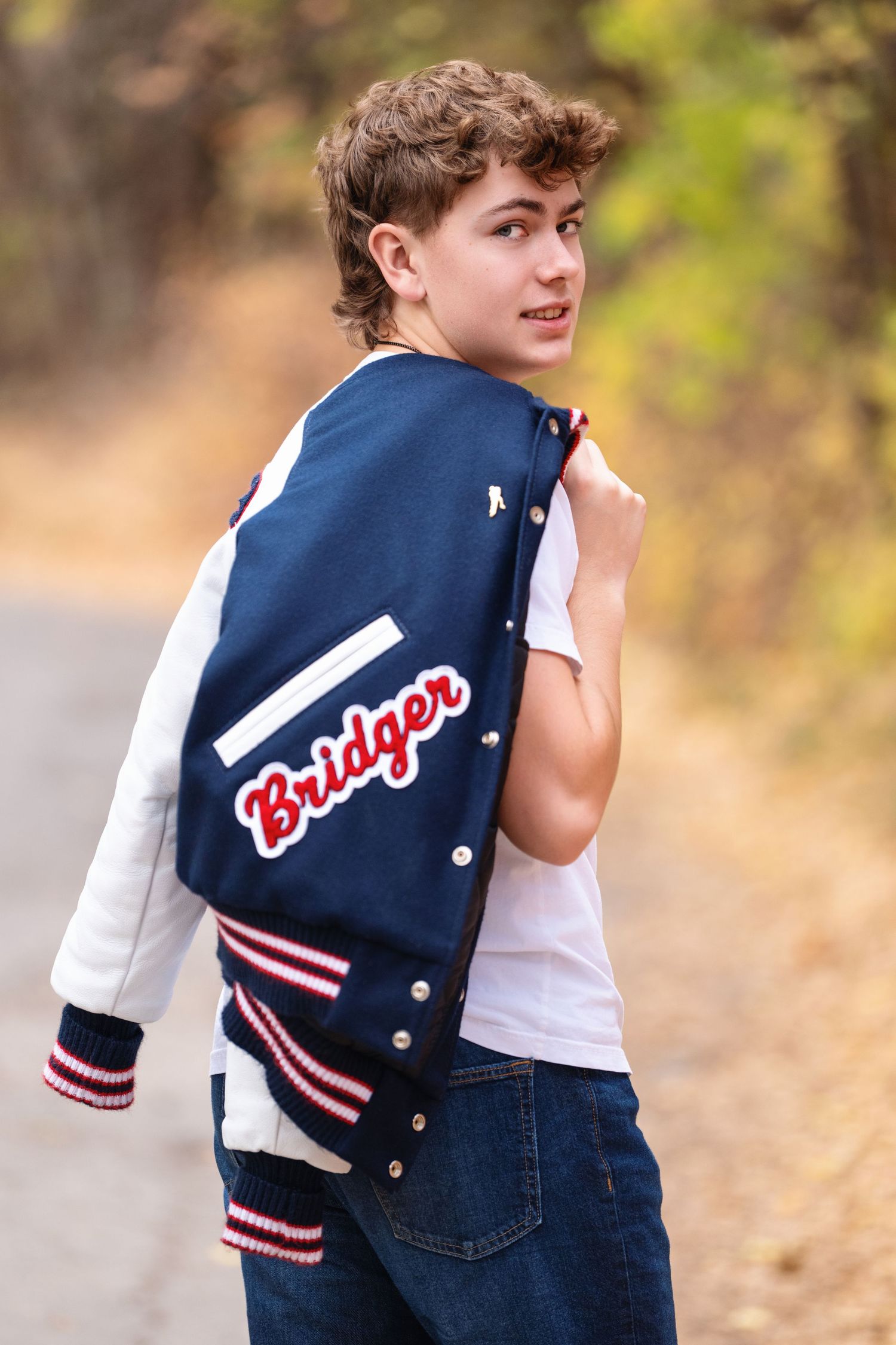 Senior boy portrait wearing letterman jacket in Mueller Park Canyon with confident over-the-shoulder pose