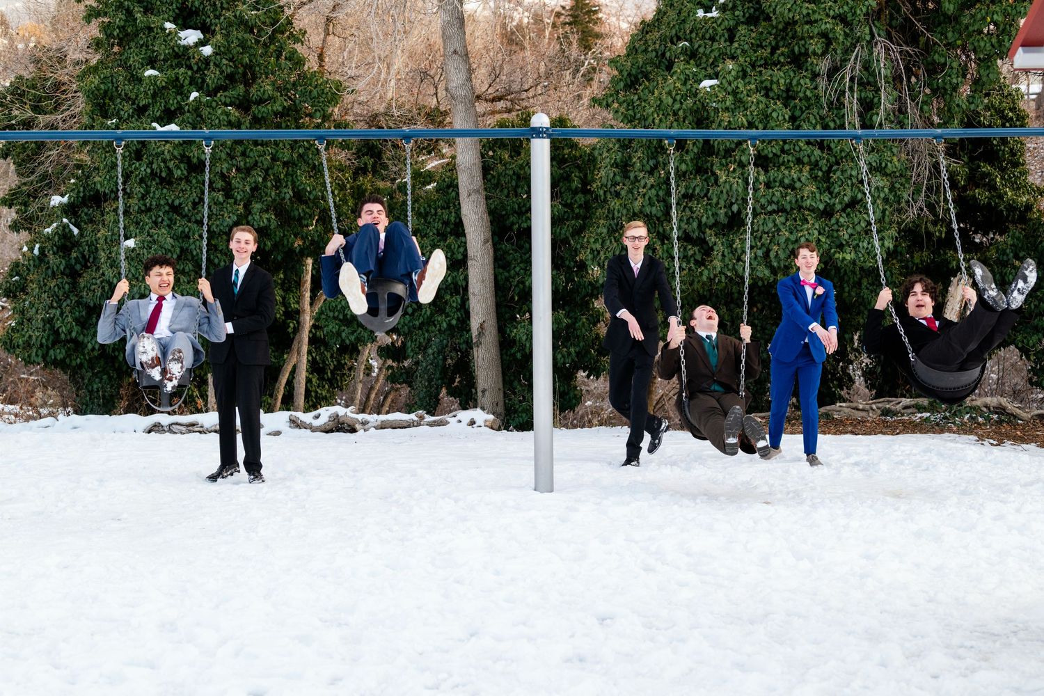 Group of boys in suits playing on swings in winter setting with snow ground before the Woods Cross Sweet Hearts dance