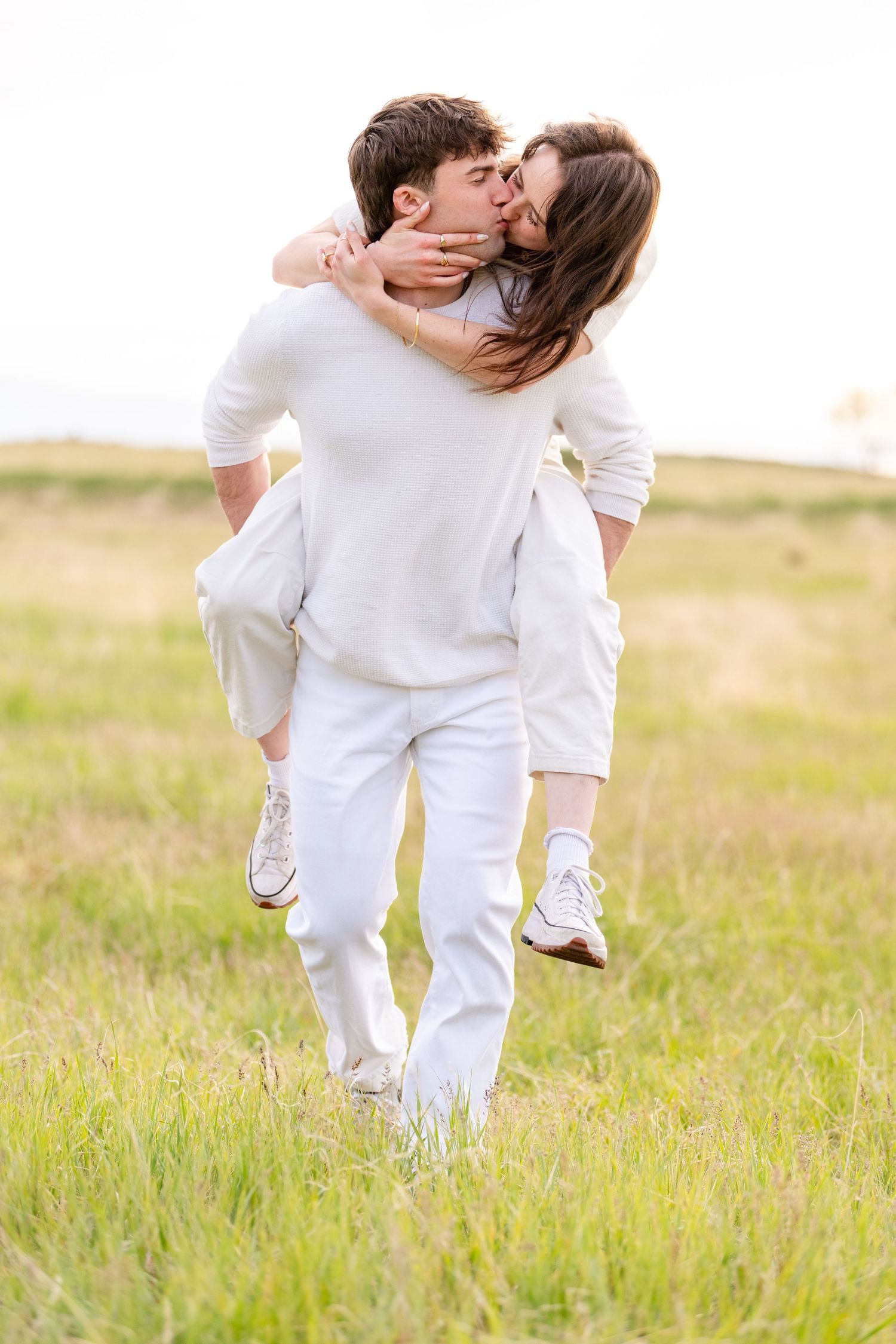 Playful engagement photo of couple piggyback riding through open field in Utah