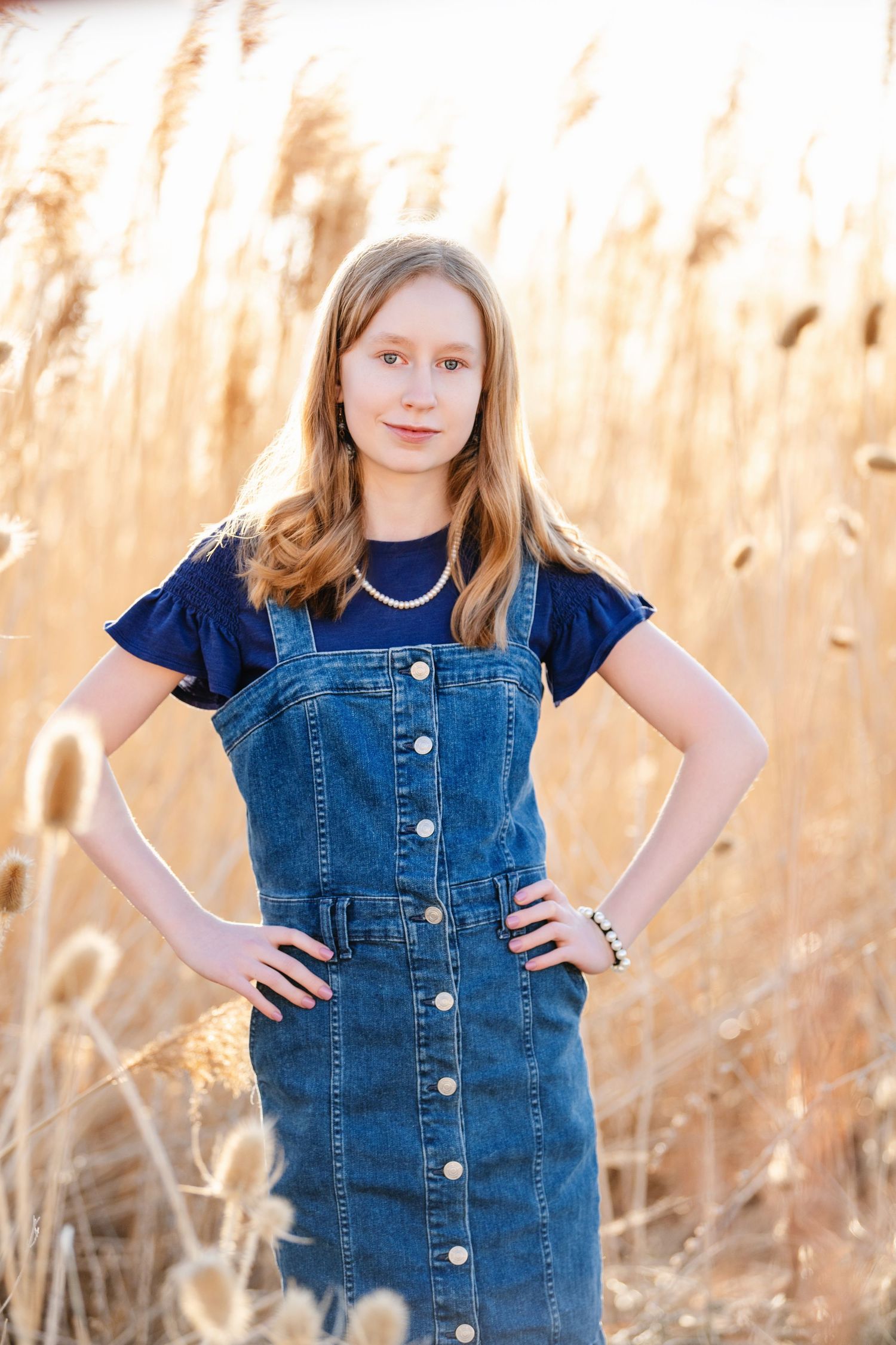 Young girl portrait in denim dress standing in tall grass during outdoor family session