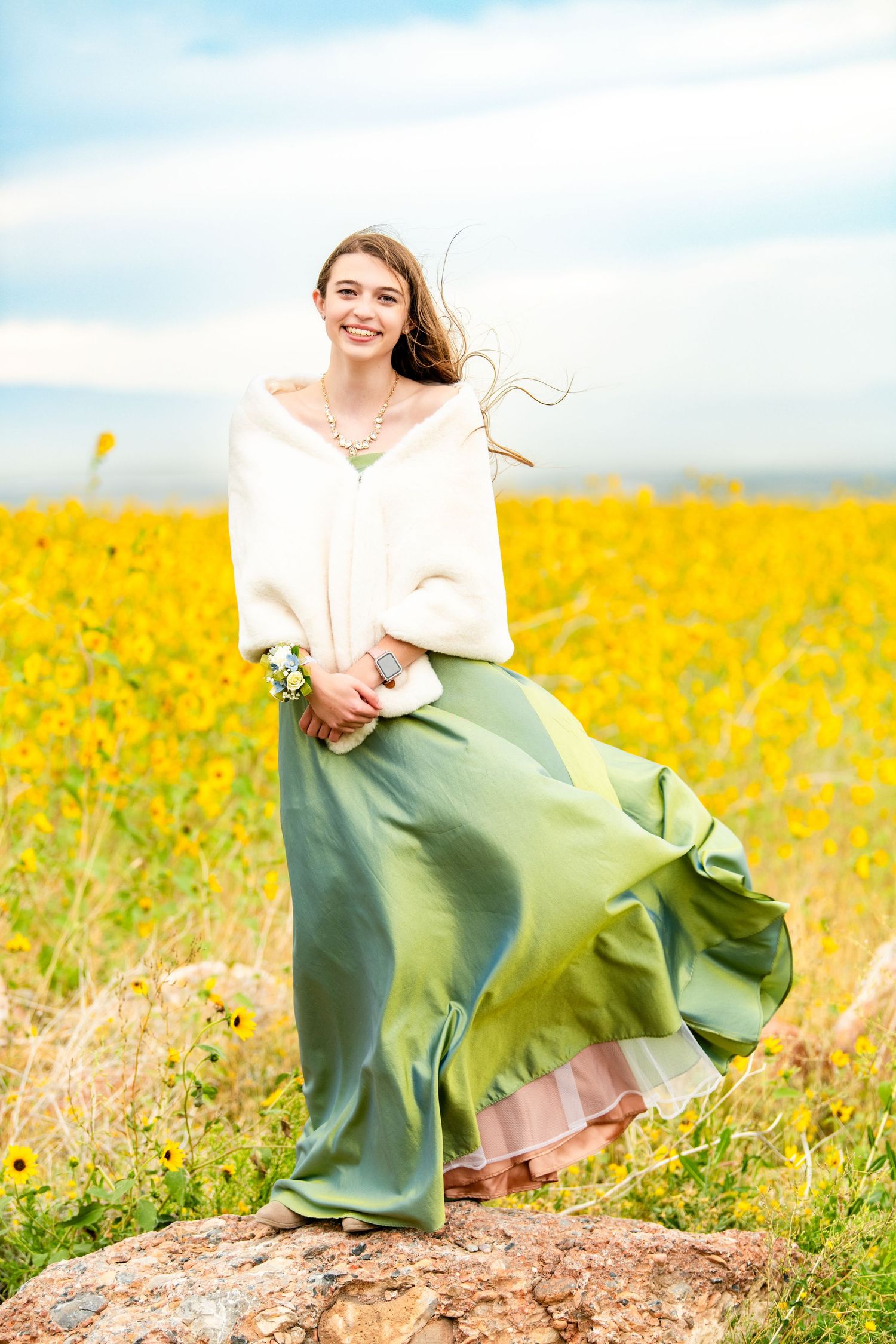 High school girl standing on rock in flowing skirt with yellow flower field backdrop