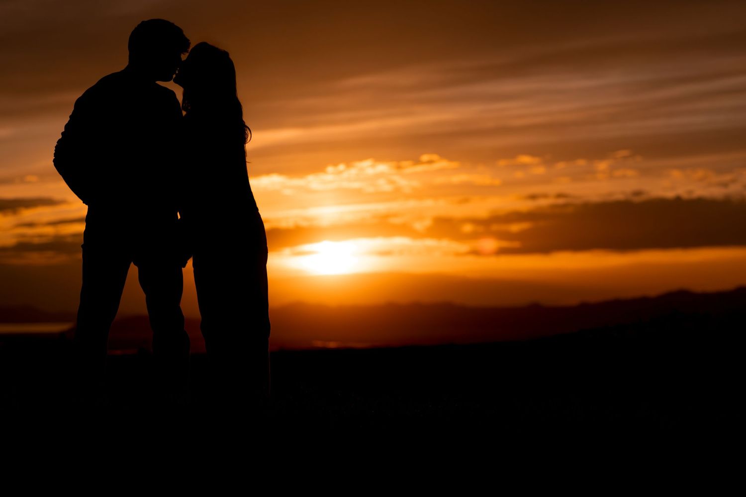 Silhouette engagement portrait at sunset with couple kissing against dramatic orange sky in Utah