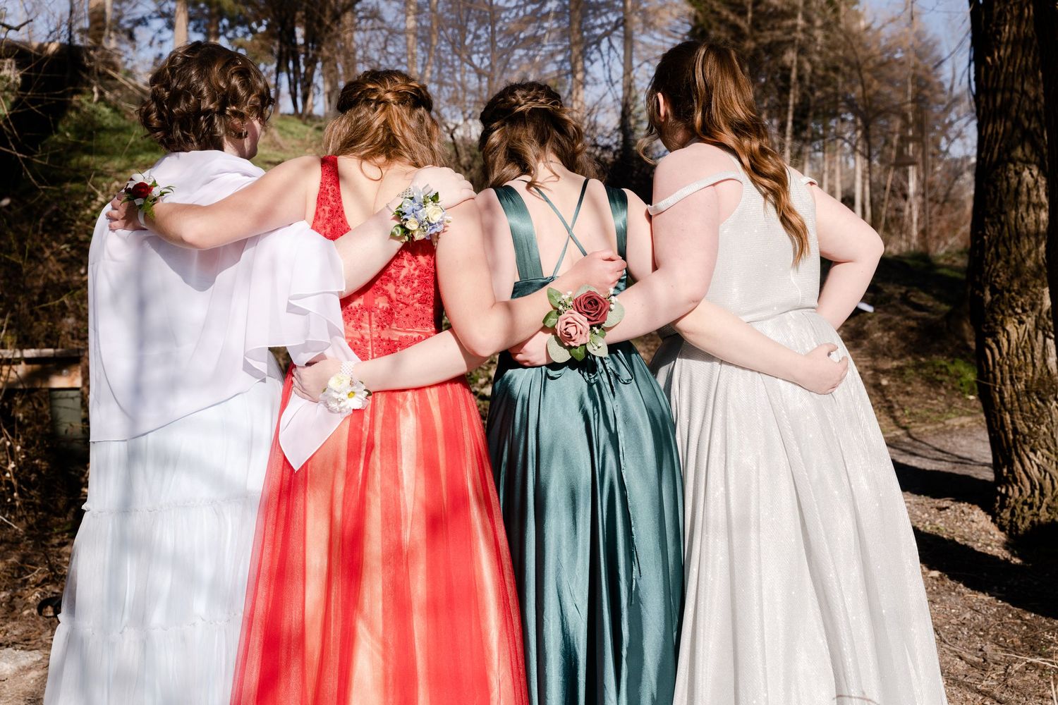 Group of girls in formal prom dresses standing together outdoors with arms around each other