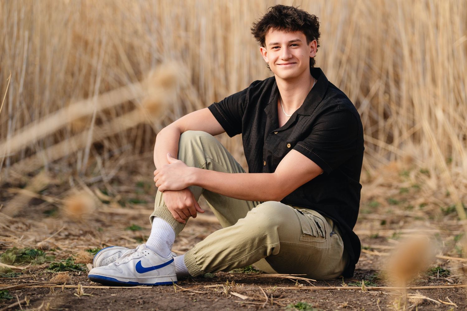 Senior boy portrait sitting in tall grass field during outdoor Class of 2025 photography session