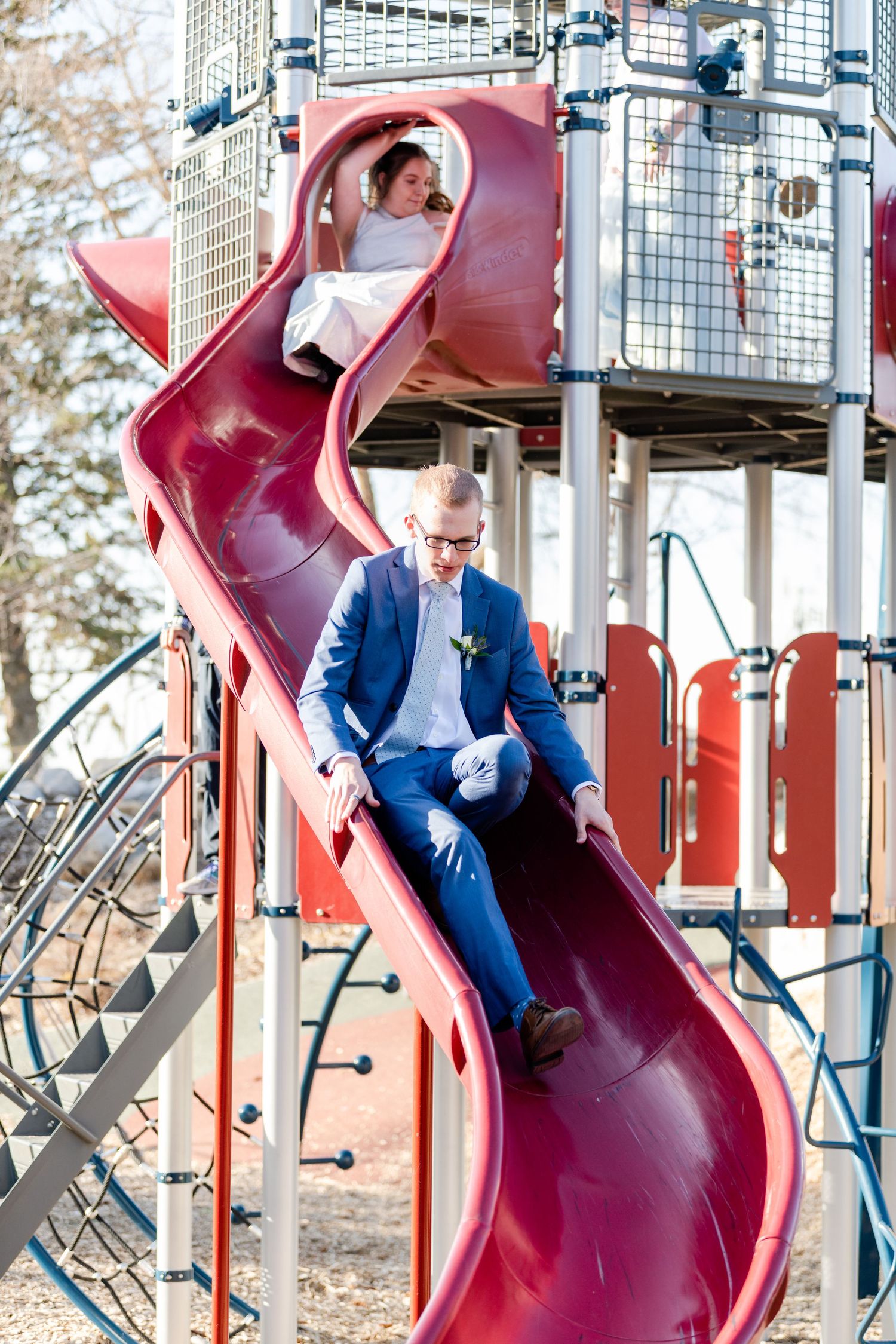 Teen boy sliding down playground slide in suit with playful prom photo concept