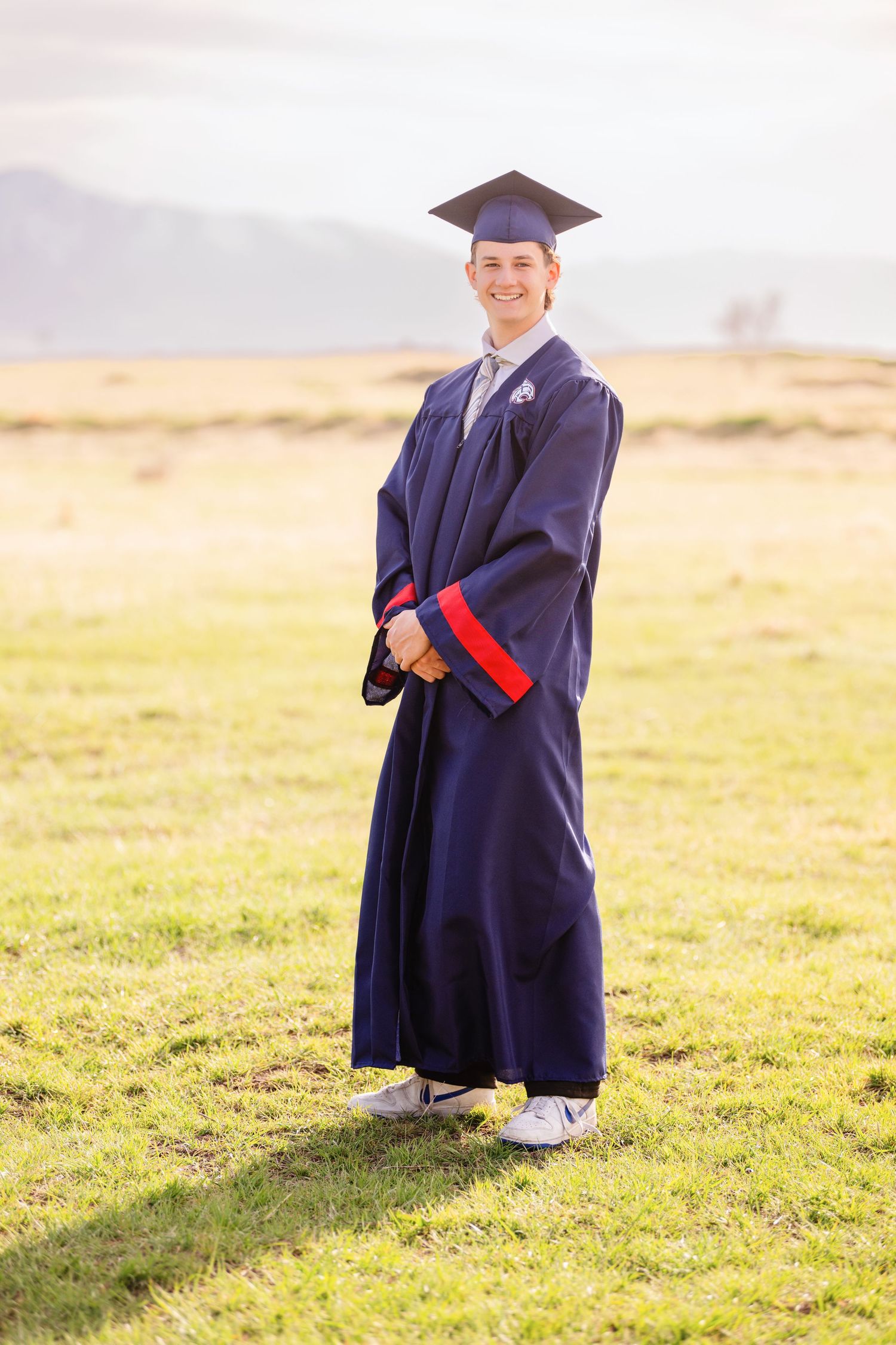 Male graduate portrait in cap and gown standing outdoors during Class of 2025 graduation session