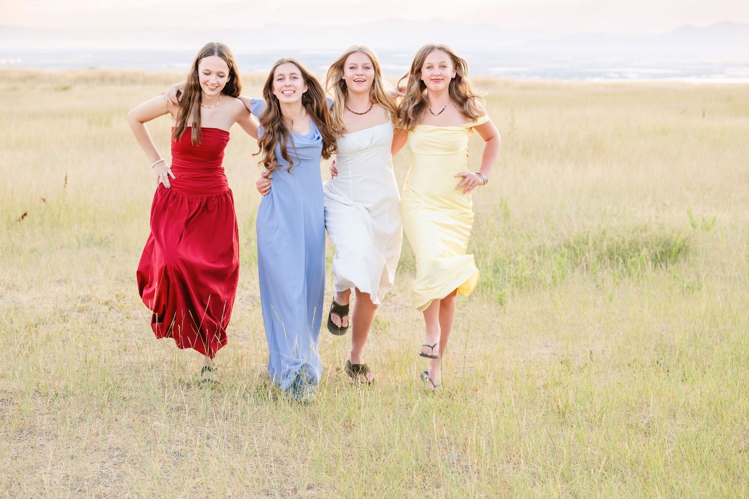 Group of high school girls walking through field in colorful dresses with joyful movement