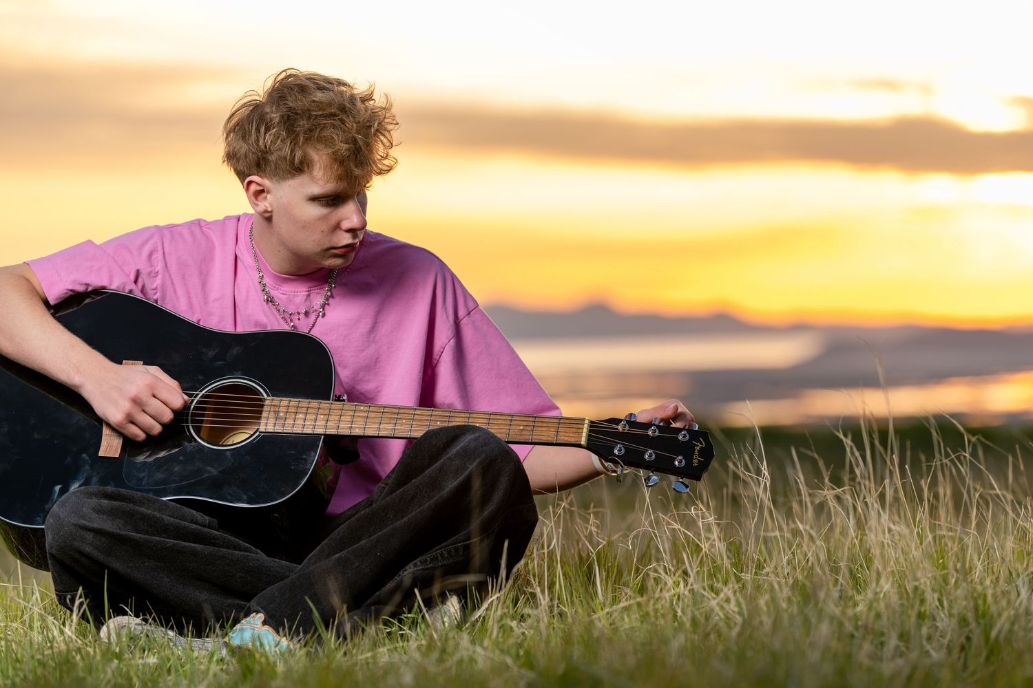 Male senior photos in Utah featuring acoustic guitar in grassy field during sunset session