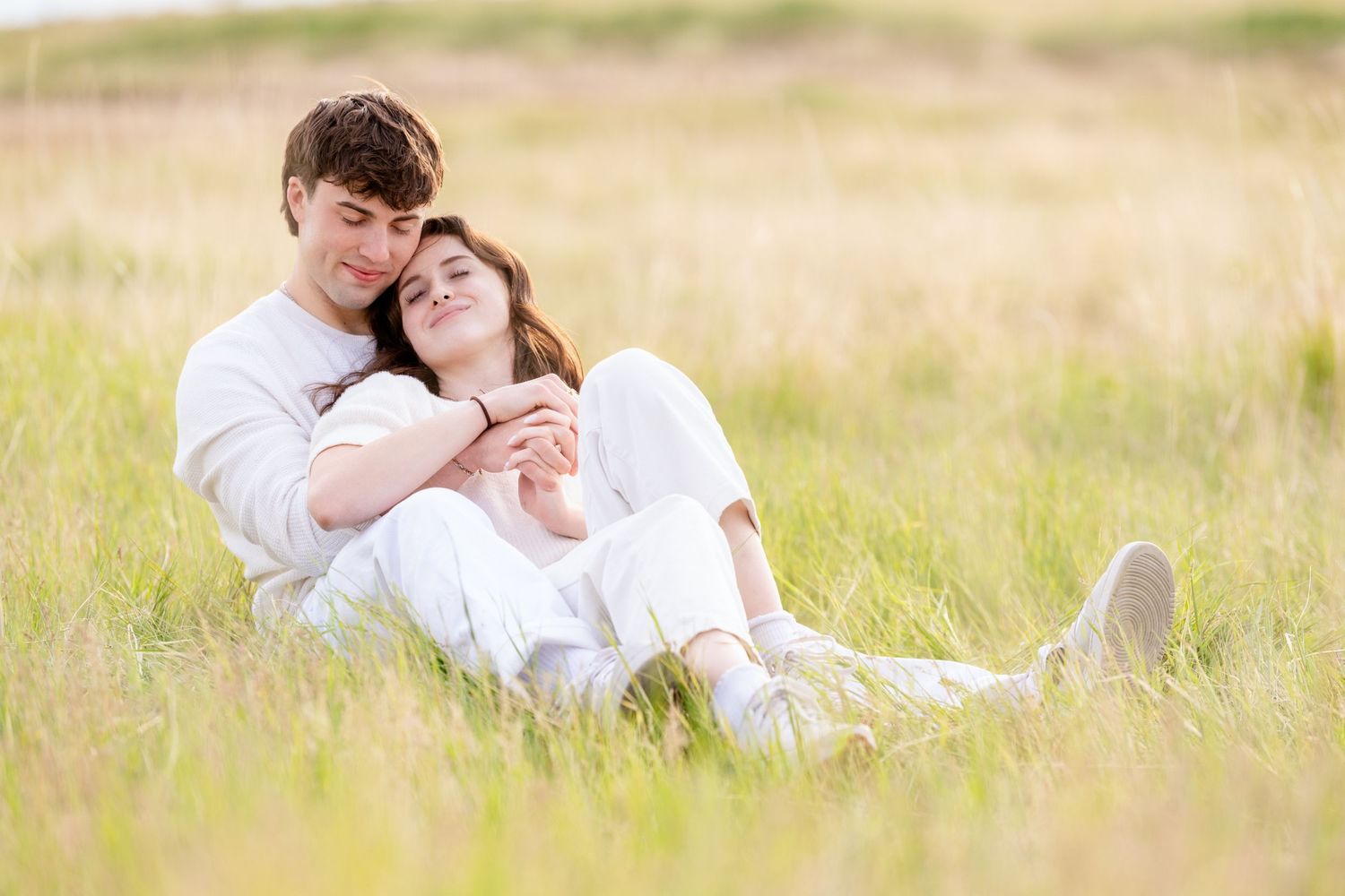 Couple cuddling in grassy field during bright and airy Utah engagement photography session