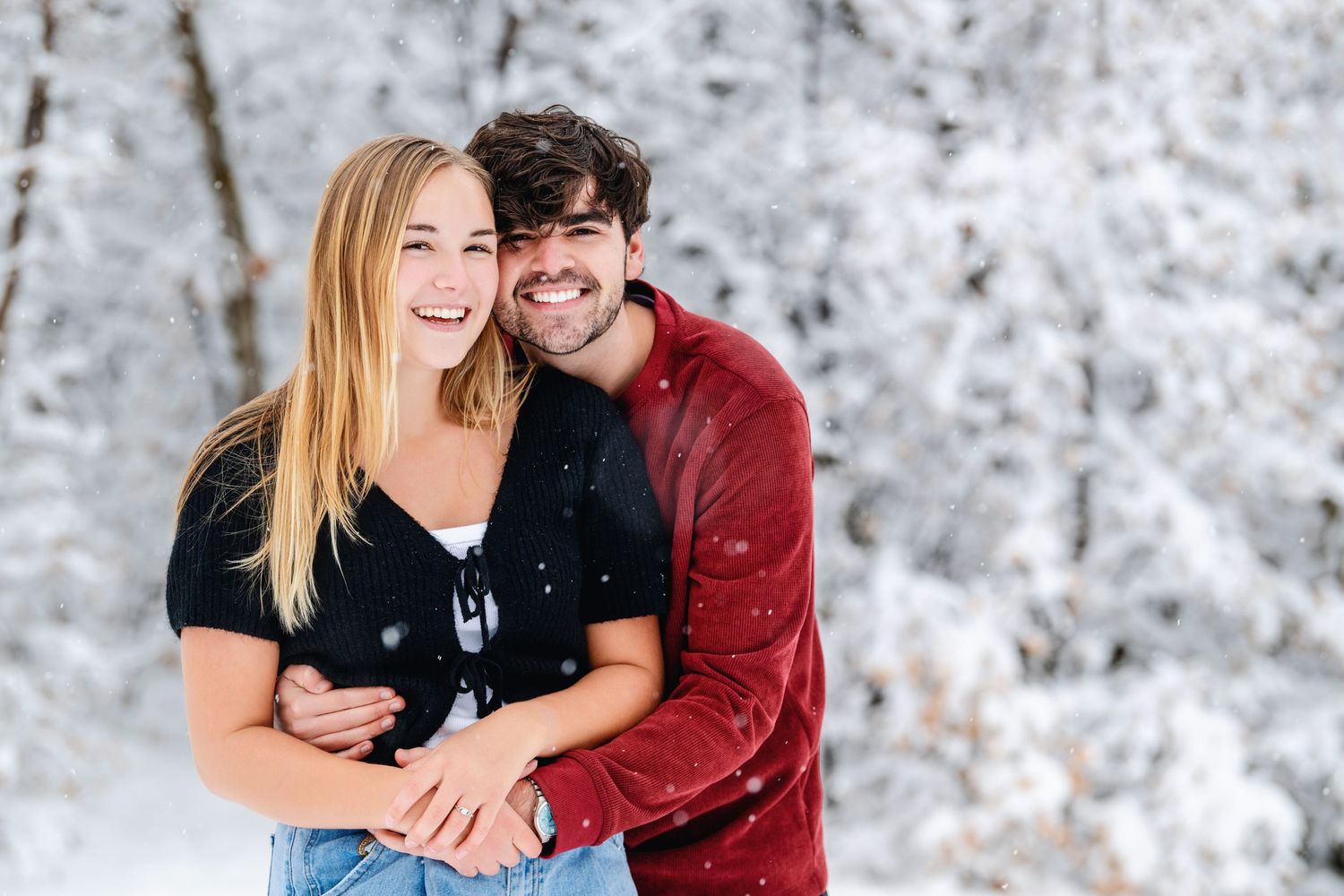 Smiling engaged couple embracing during snowy winter engagement photography session