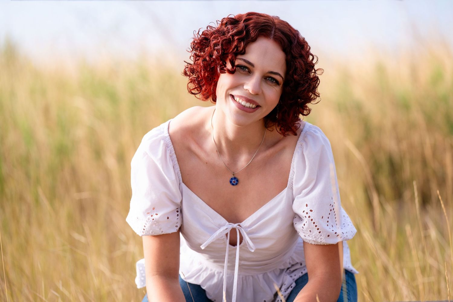 Young female with red tinted hair and side lighting casually sitting down looking directly into the camera while smiling.
