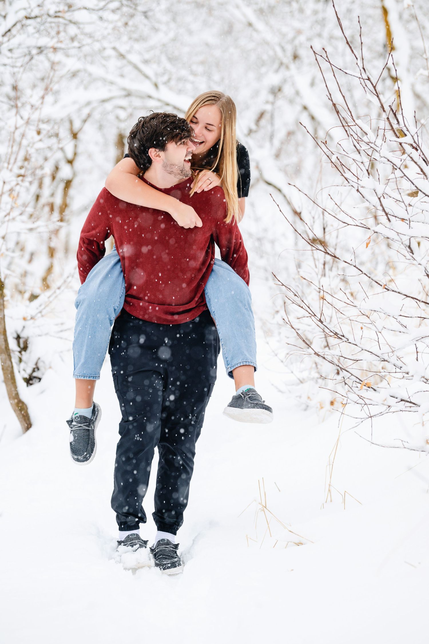 Winter engagement photo of man carrying fiancée through snowy trees during outdoor session