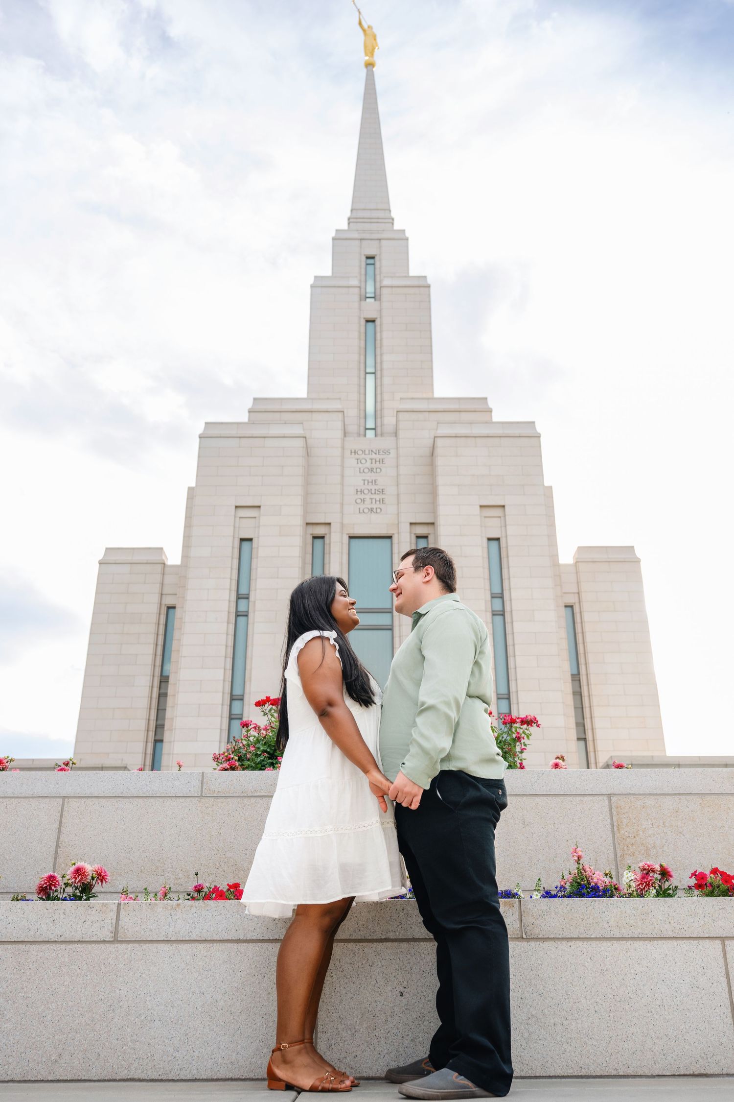 Couple standing in front of LDS temple holding hands in soft light during engagement session