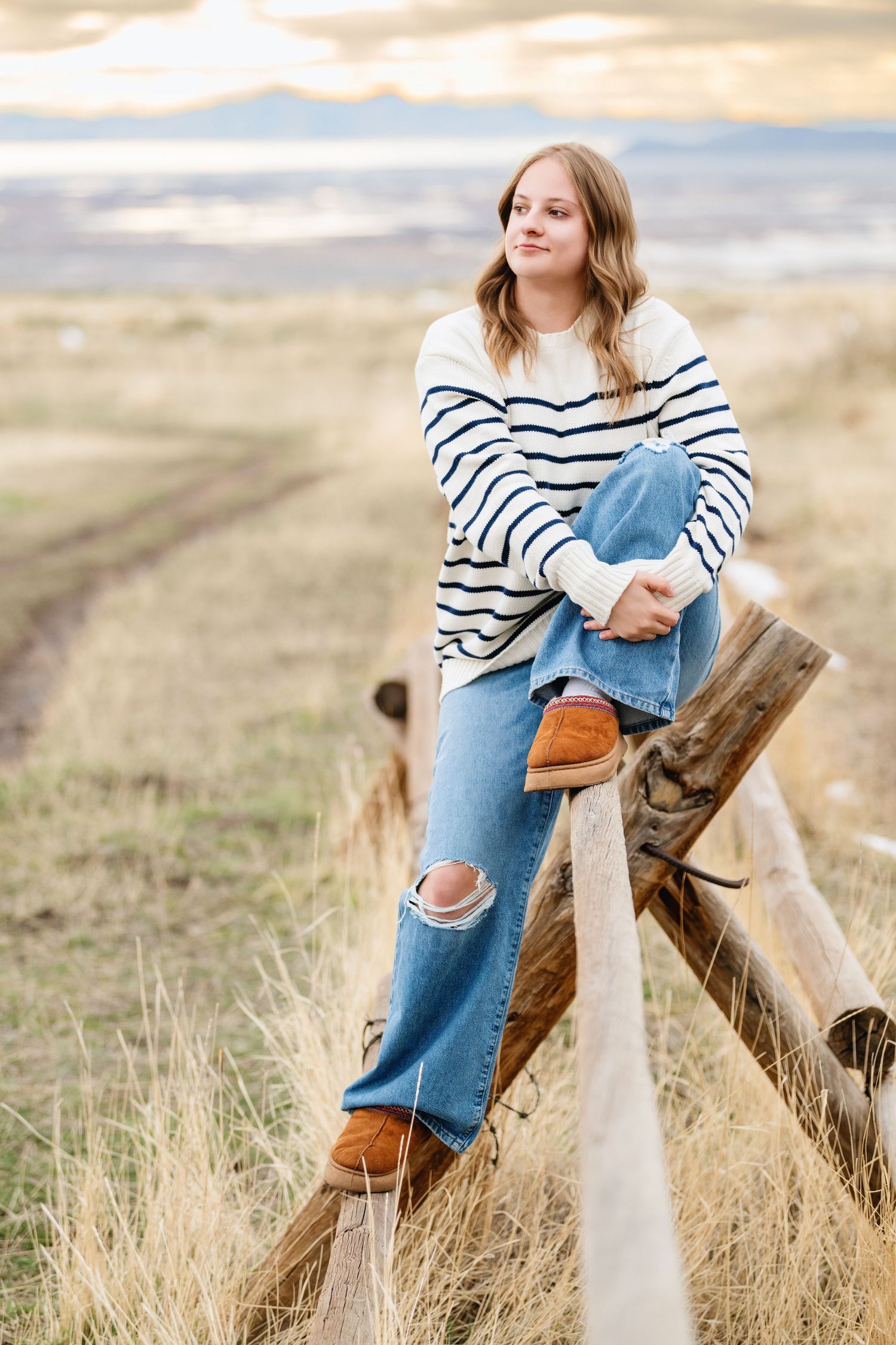 Outdoor senior girl portrait sitting on rustic fence in open Utah field during golden hour