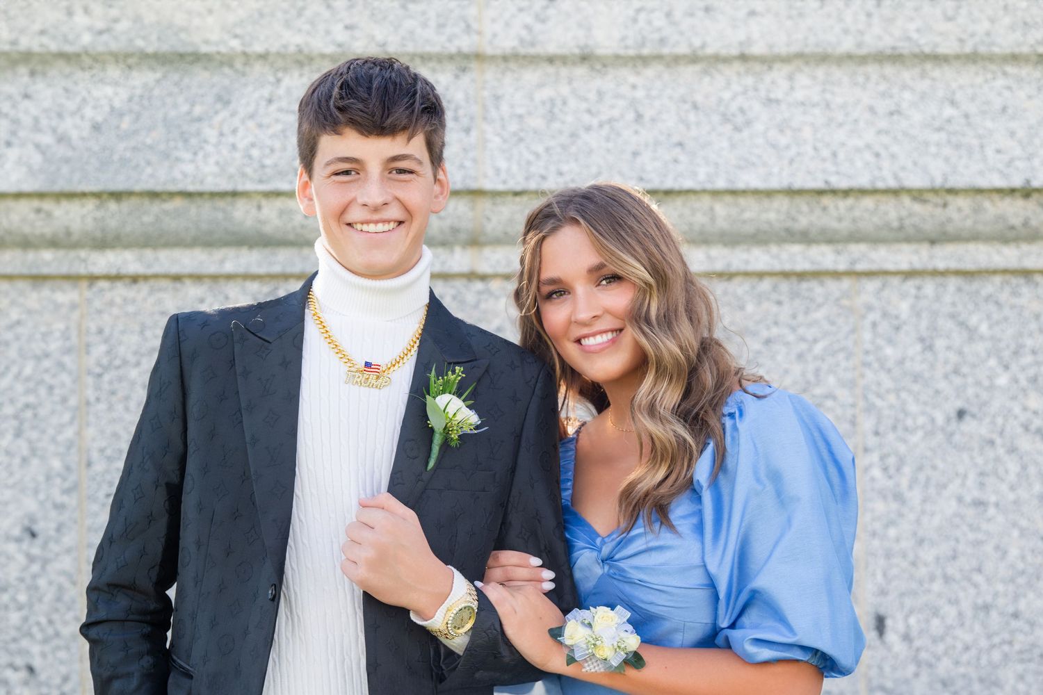 Couple portrait smiling together with blue dress and black suit against stone wall