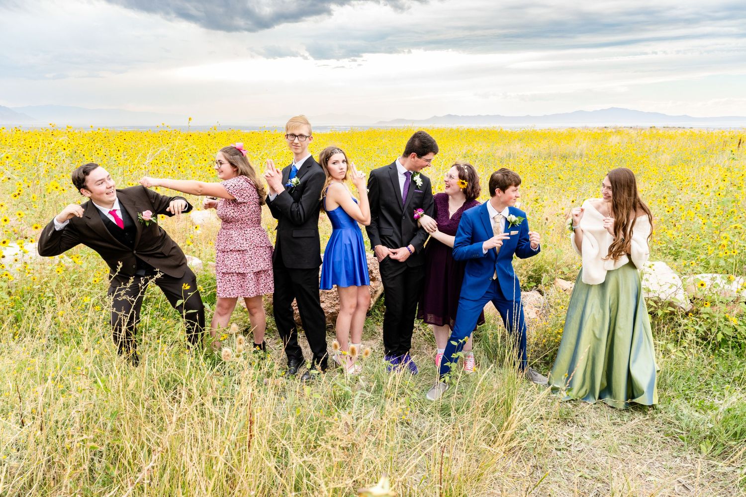 Group of teens in formalwear posing in yellow flower field with playful expressions for the Woods Cross homecoming dance