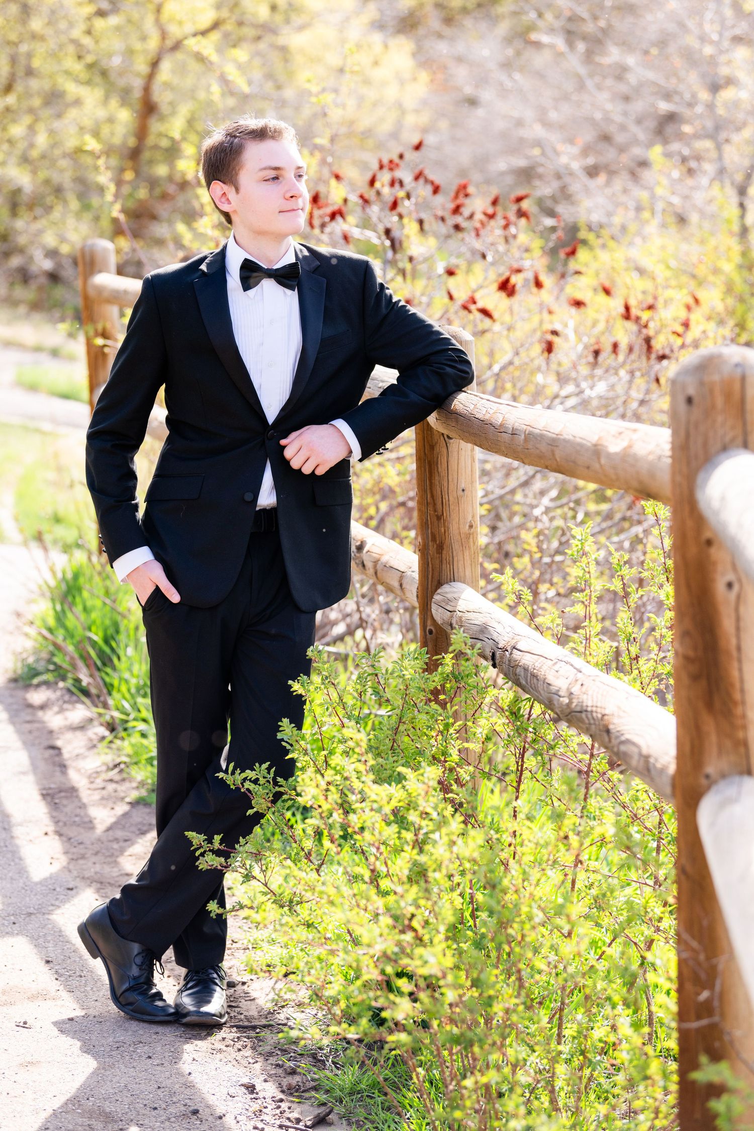Senior boy portrait leaning on fence in tuxedo with natural outdoor background