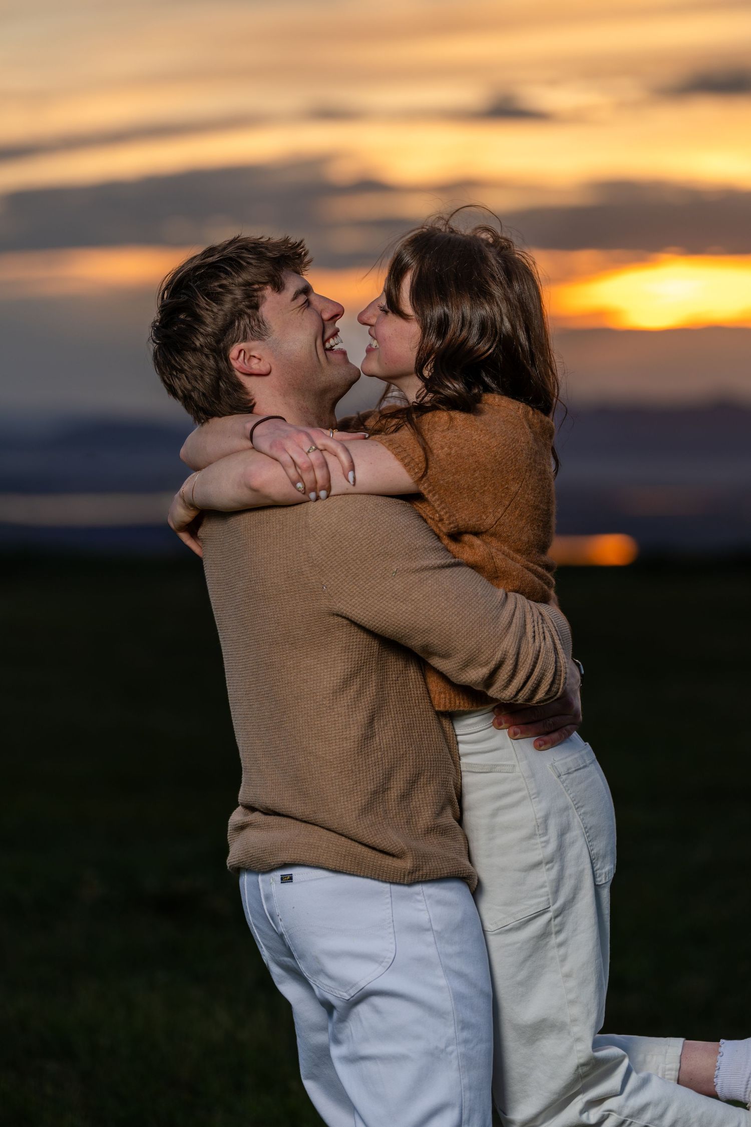Utah engagement couple embracing at sunset in open field during golden hour photography session.