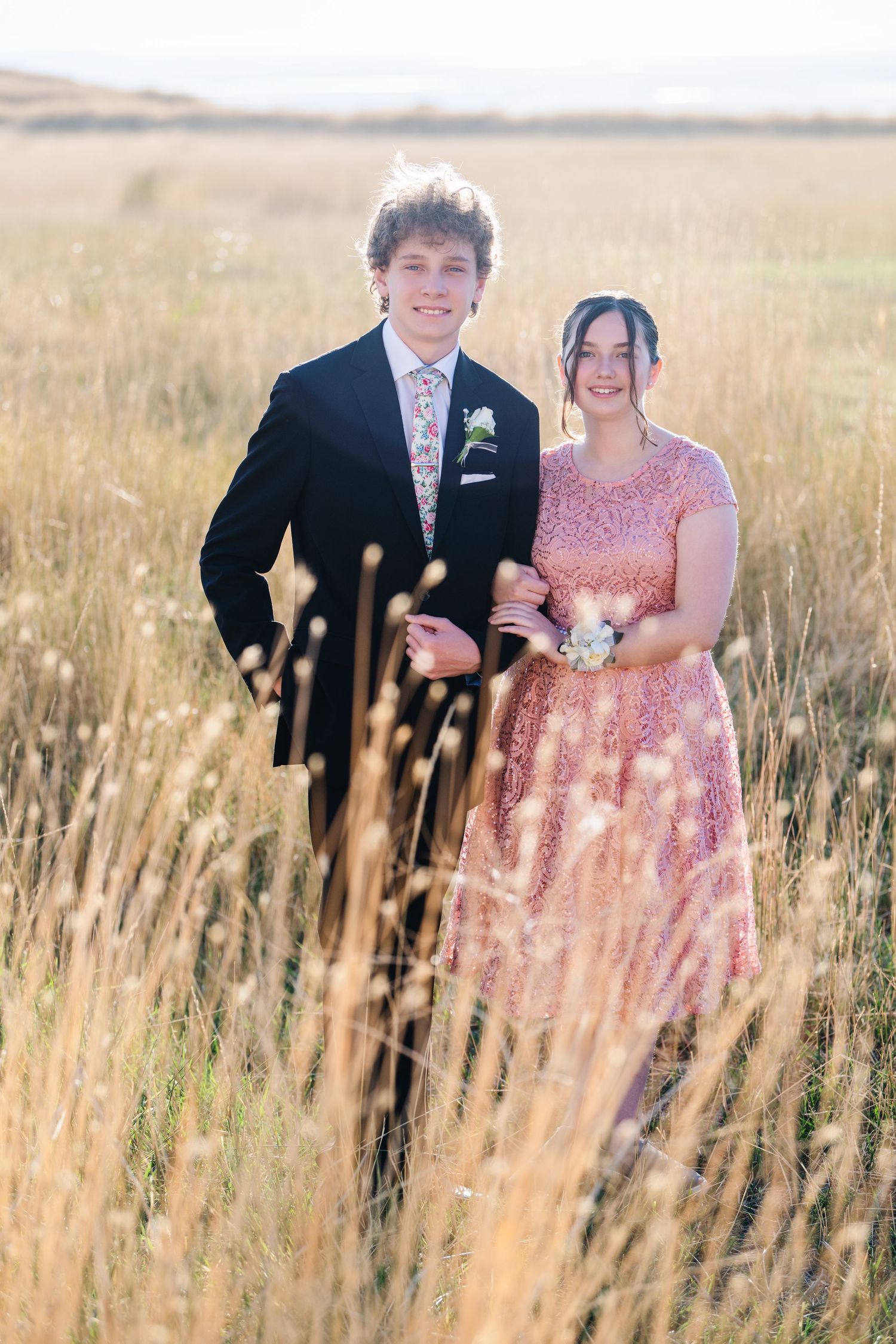 Woods Cross High School couple standing in tall grass field in formal attire with soft natural tones