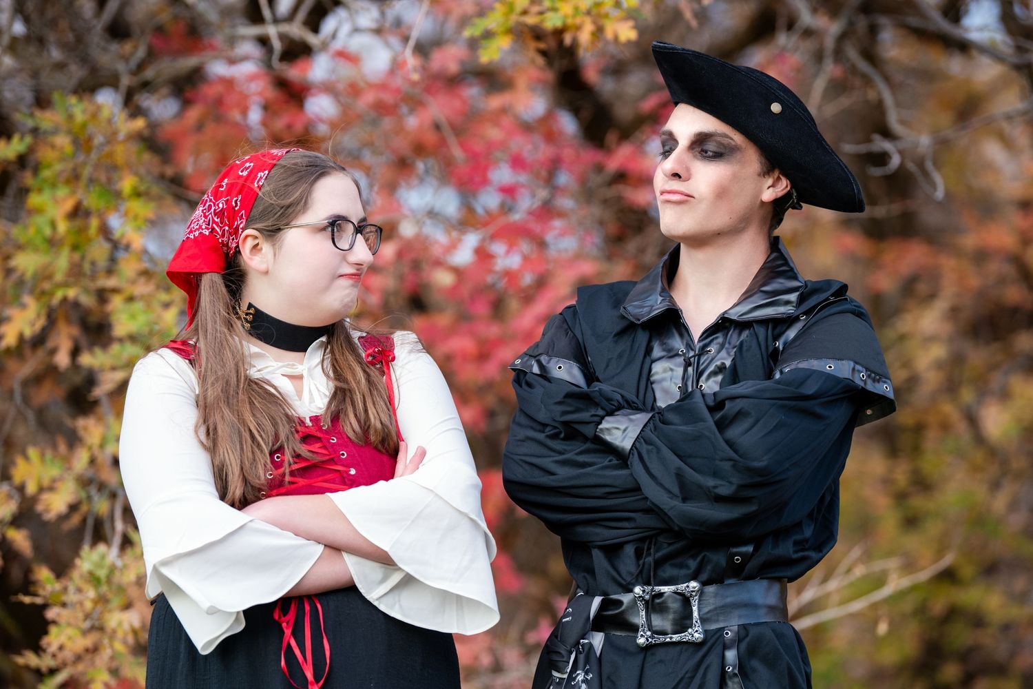 Two teens in pirate themed outfits posing with crossed arms and fall leaves behind