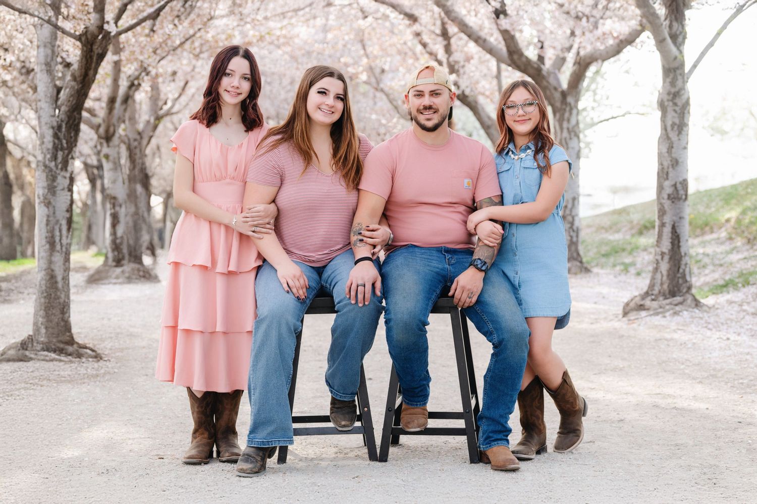 Family portrait with parents and daughters sitting together beneath blossoming cherry trees