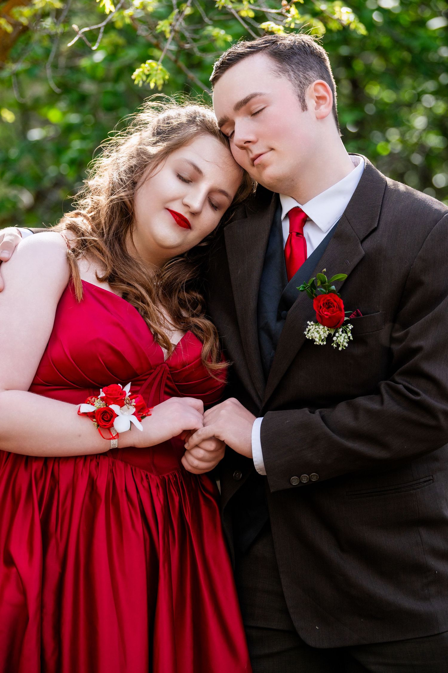Close-up prom couple portrait with red dress and black suit in soft greenery