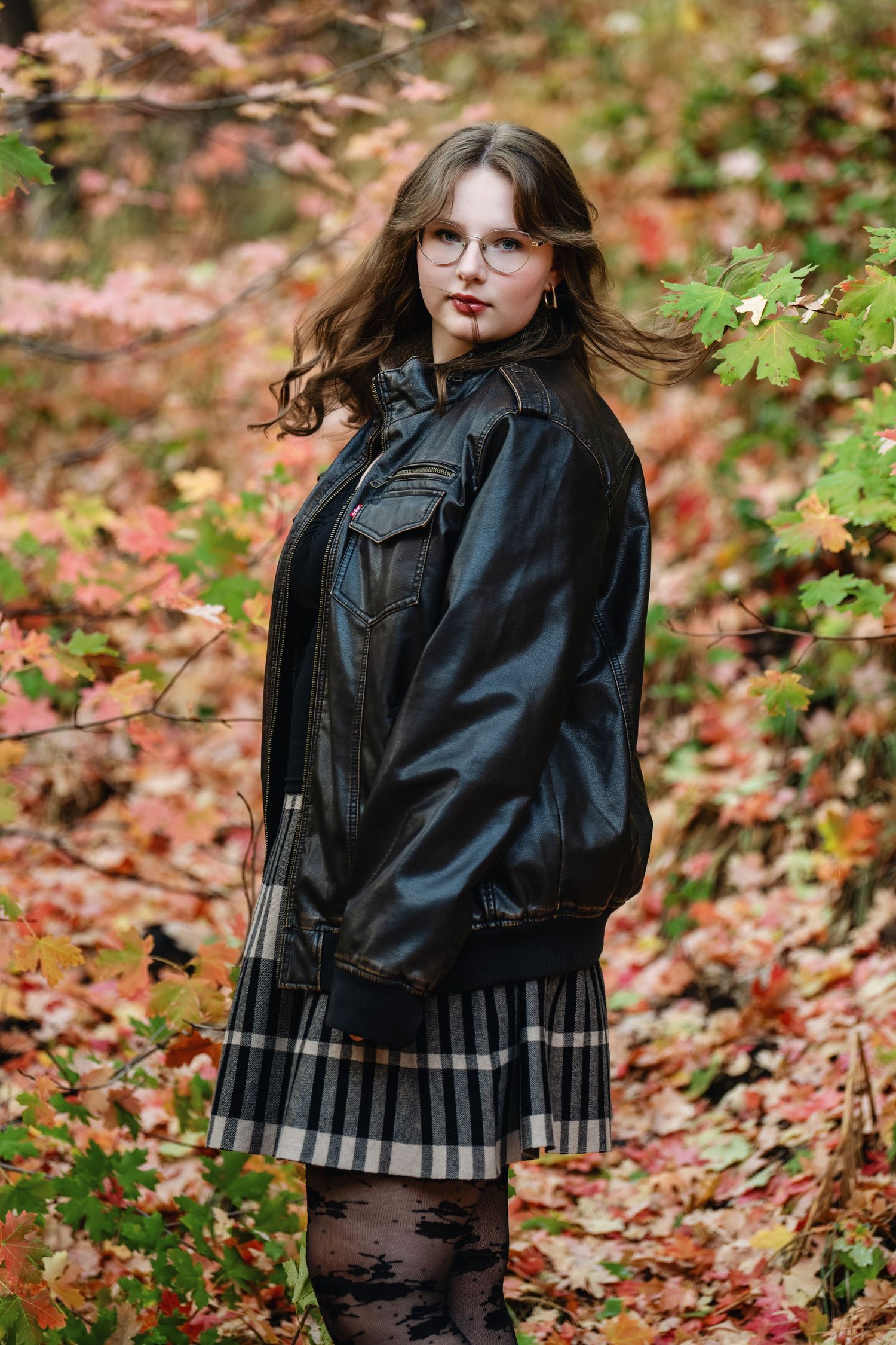 Senior girl portrait in fall leaves wearing black leather jacket with bold confident expression