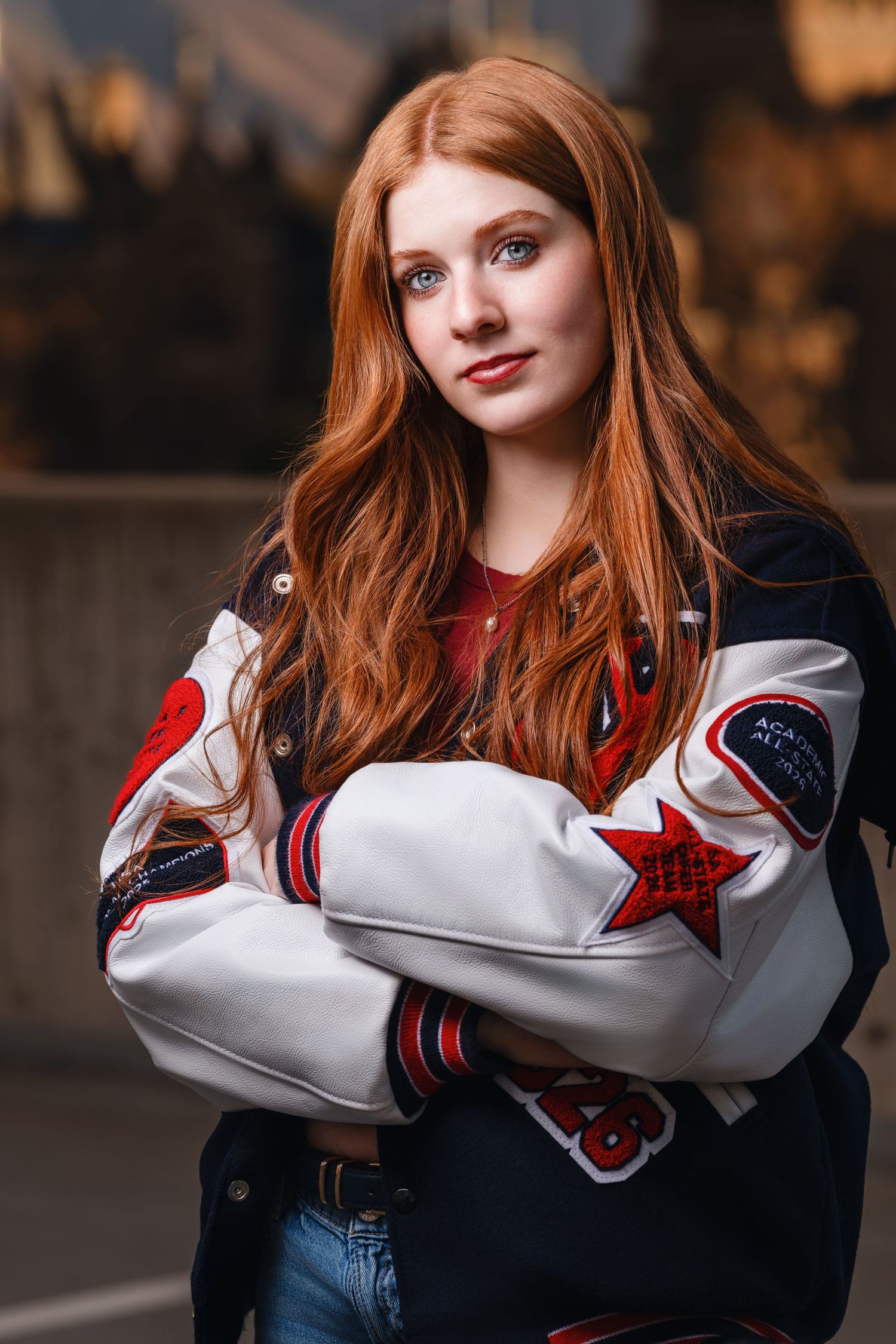Senior girl portraitwith red hair  in Salt Lake City wearing letterman jacket in warm evening light with confident expression
