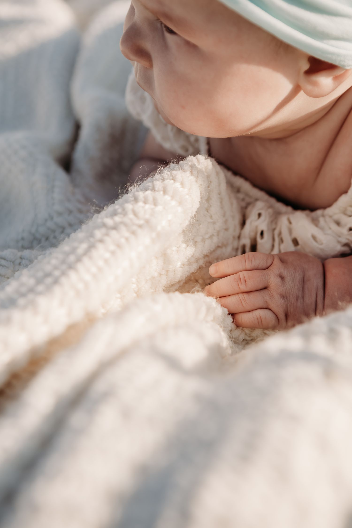 Close up of a baby in white lace clothing and soft hat resting on delicate fabric in natural light.