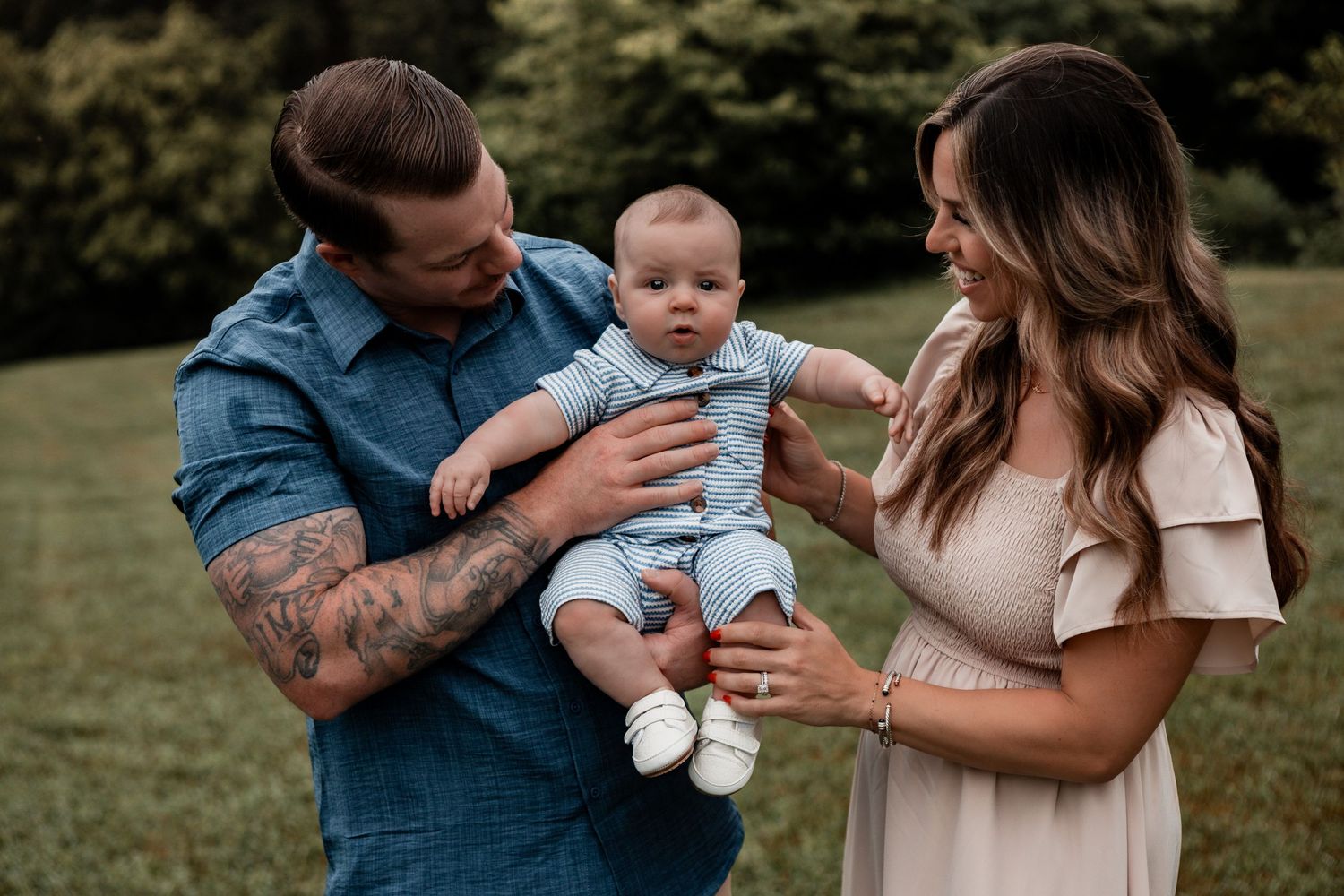 Family photoshoot in a park showing playful interactions between parents and baby in coordinated outfits.