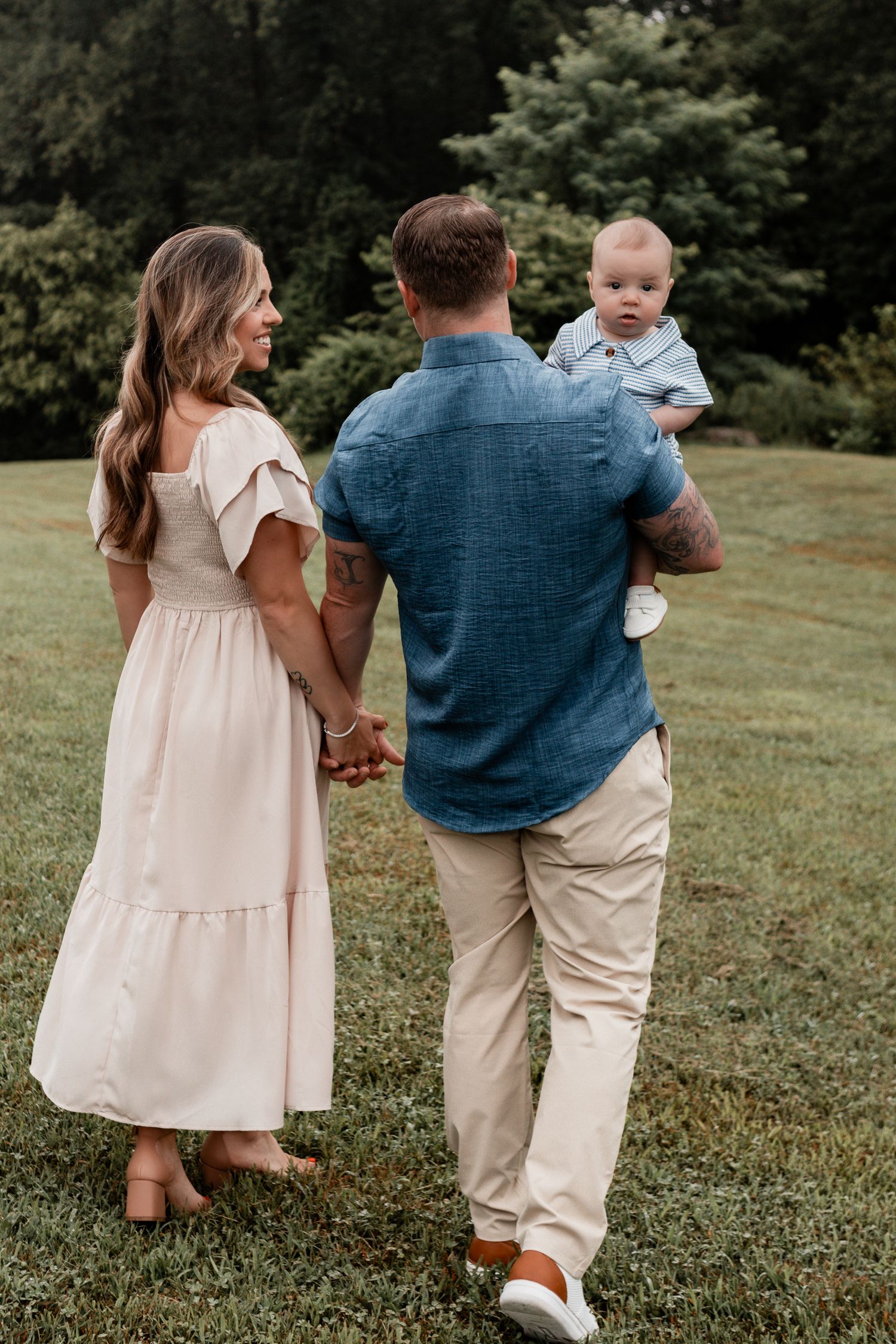 A family stands together outdoors on grass, with a denim shirt, white dress, and small child in casual attire.