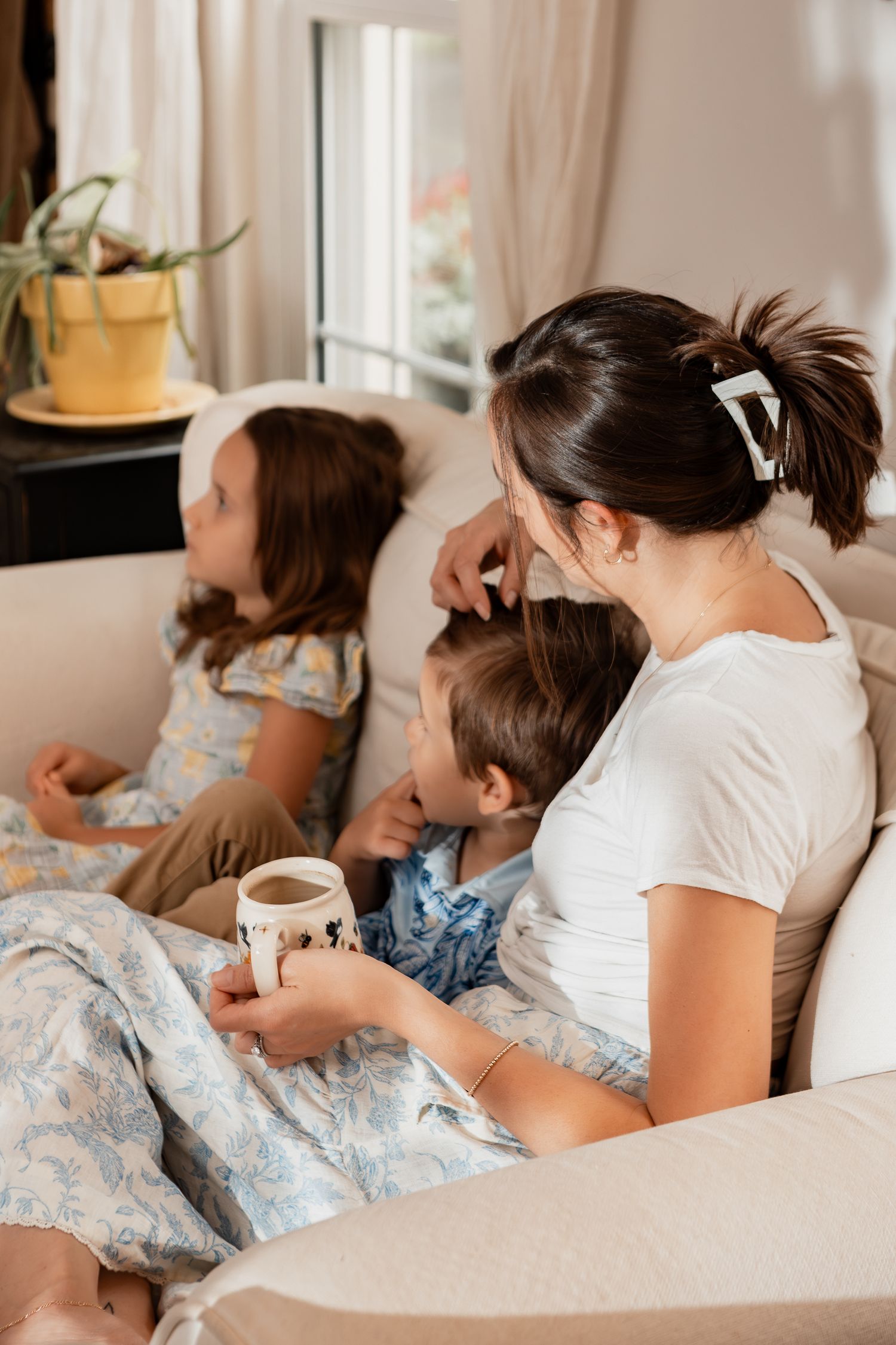 A cozy morning scene of a parent and children relaxing together on a sofa with coffee and natural light streaming in.