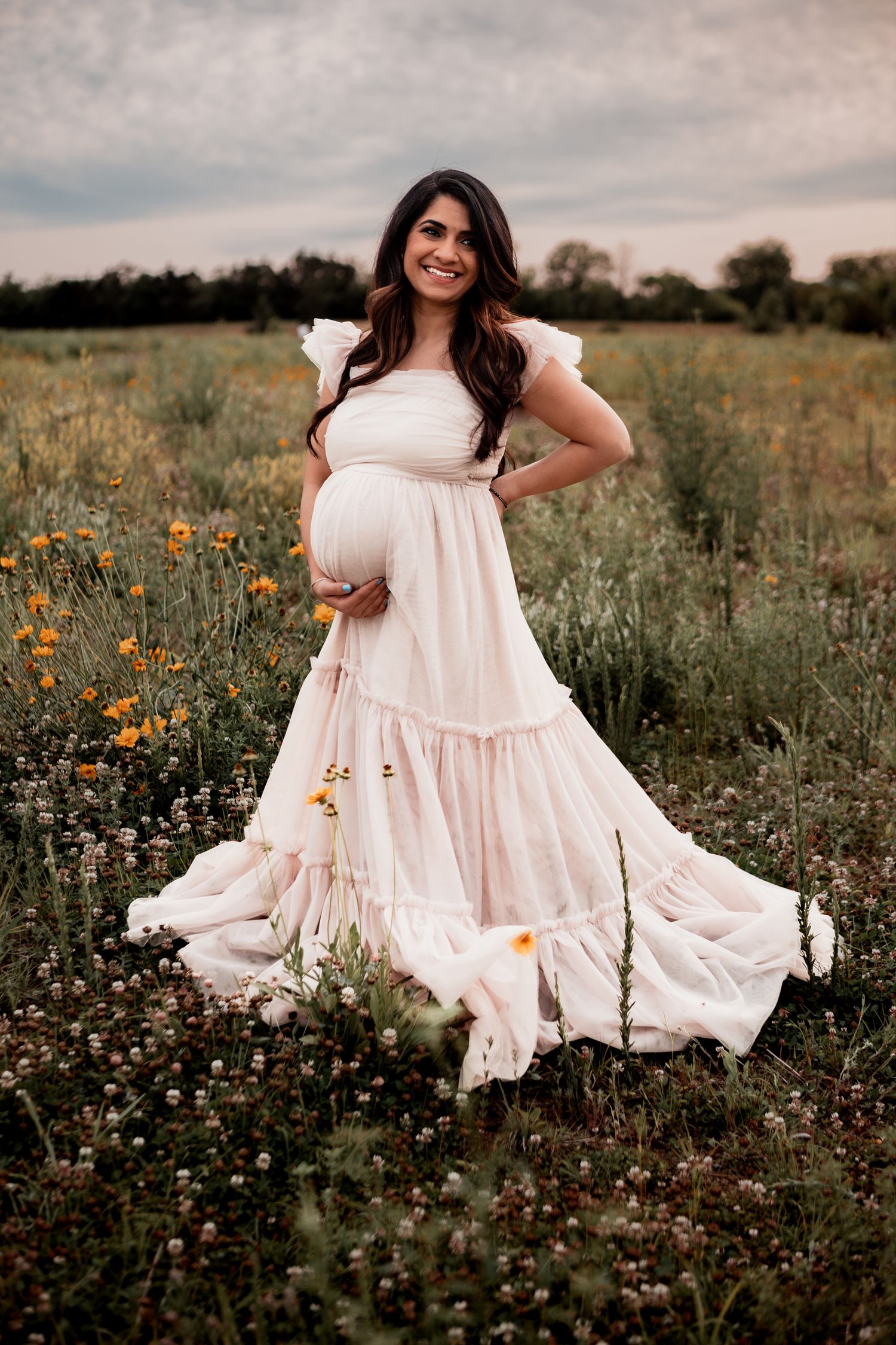 A person in a flowing white dress twirls gracefully in a wildflower meadow at sunset.