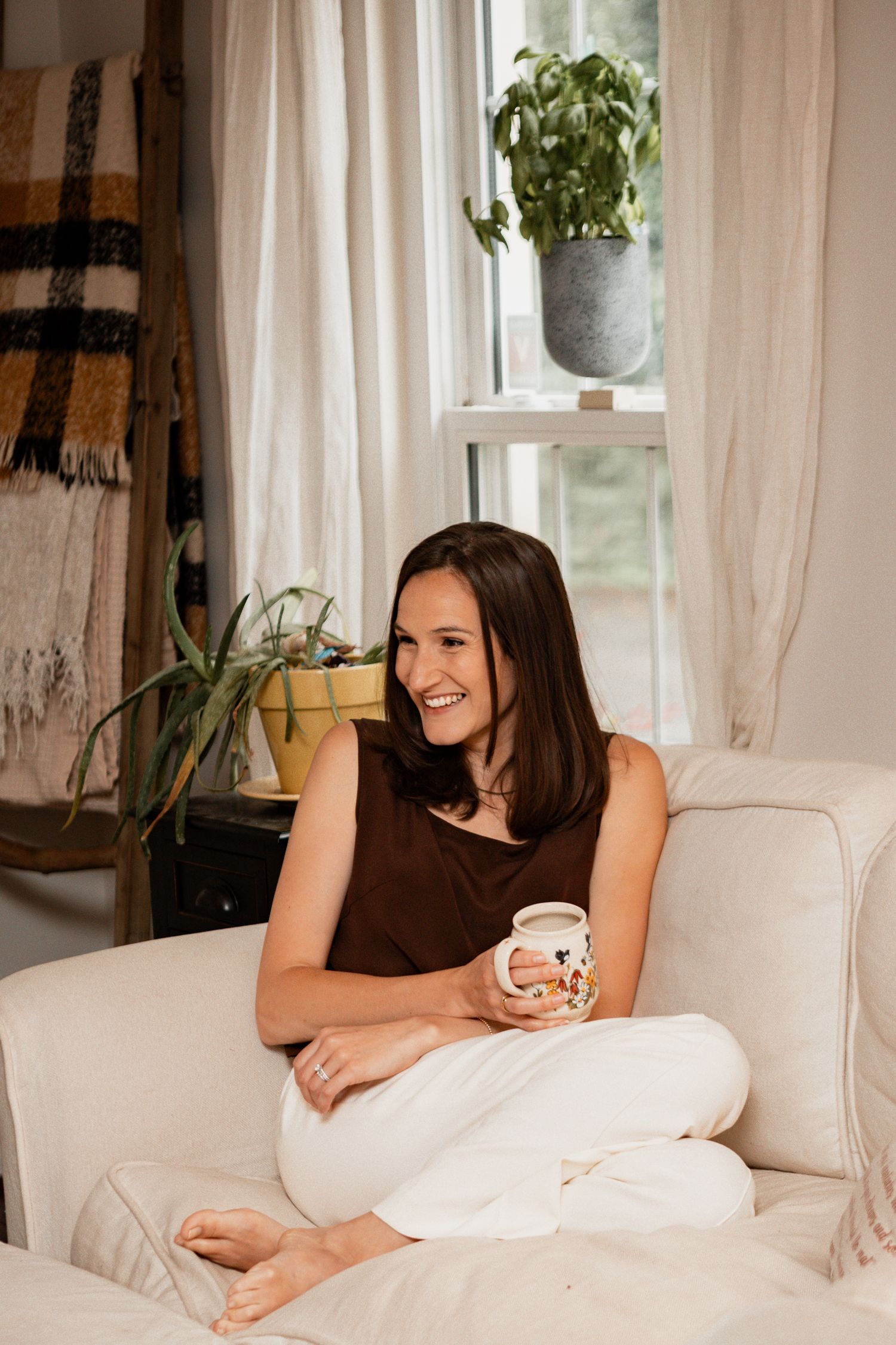Person lounging comfortably on white couch in bright sunlit room with houseplants and curtains.