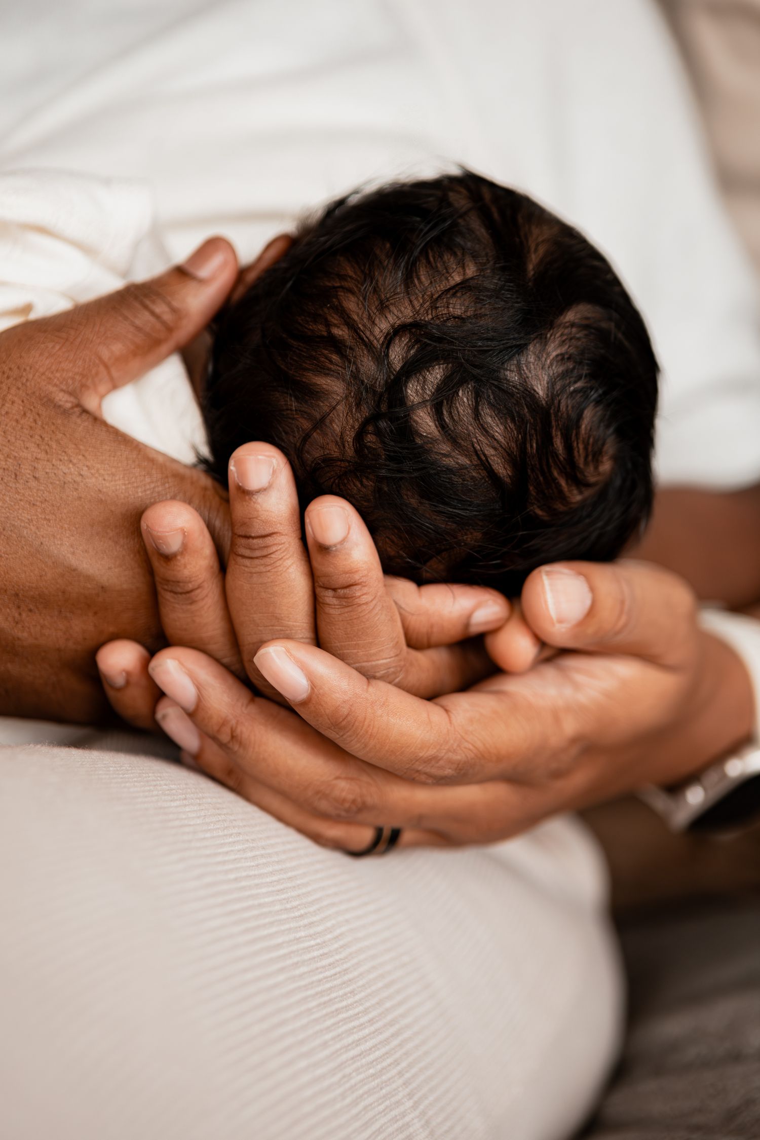Gentle hands cradle a sleeping newborn baby's head against soft white bedding.