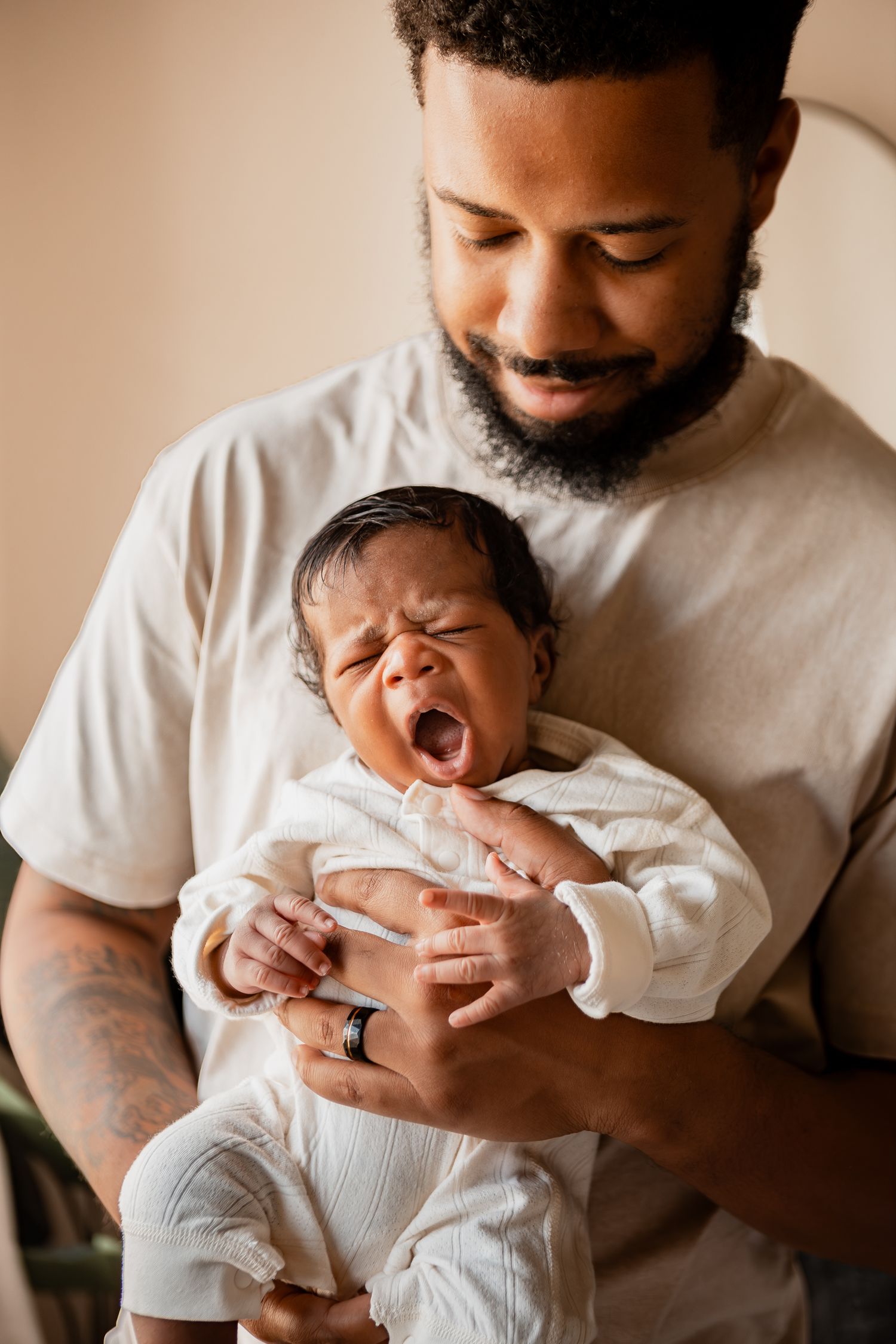Collage of four intimate moments showing a parent cradling a yawning newborn baby in a white onesie.