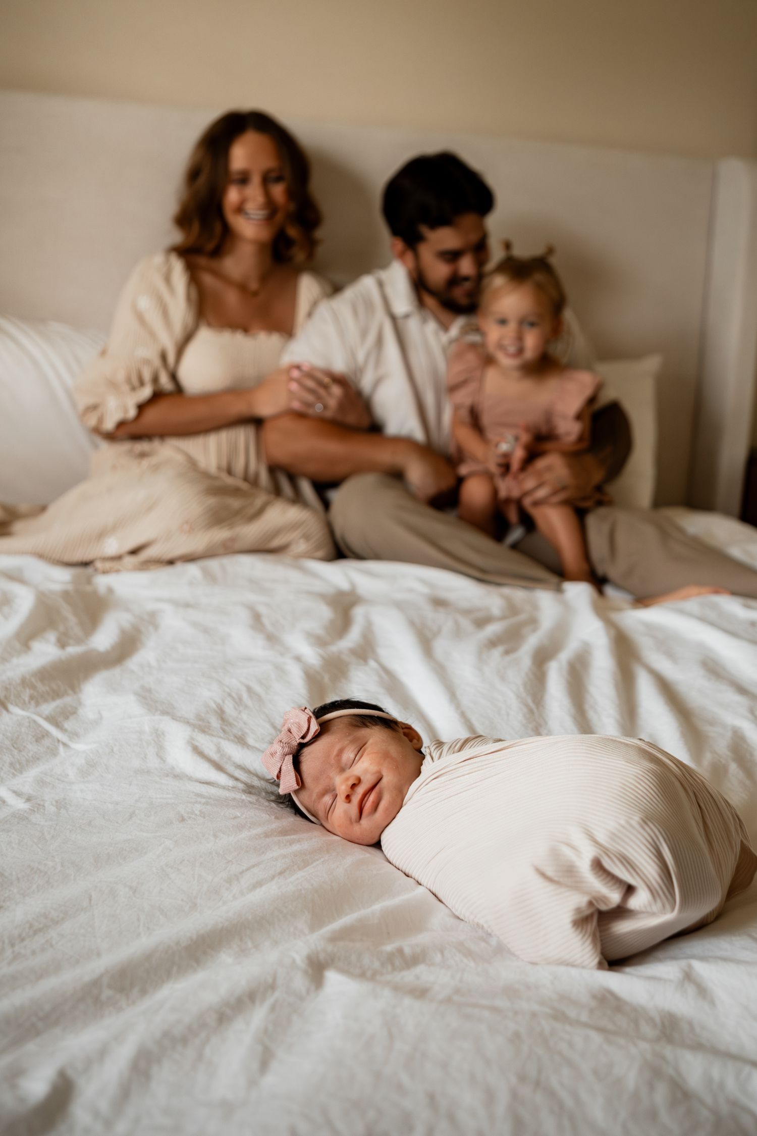 Series of lifestyle photos showing tender moments of family and sleeping baby on white bedding.