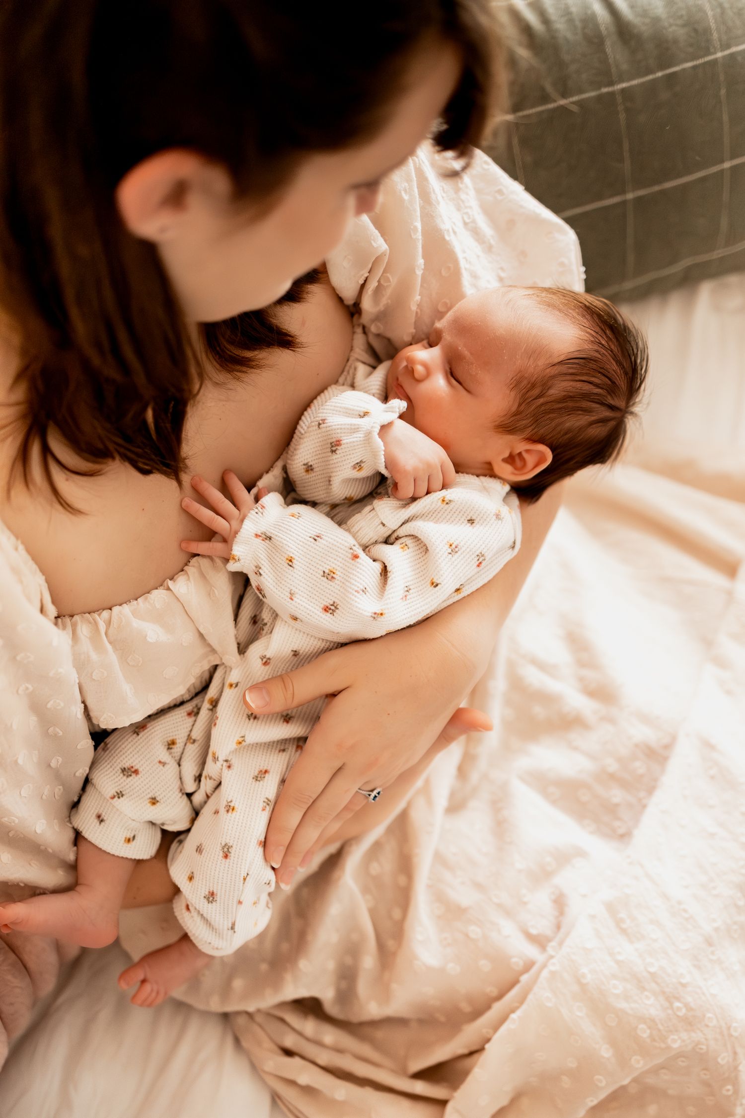 A tender moment between parent and sleeping newborn baby in polka dot sleepwear on soft bedding.