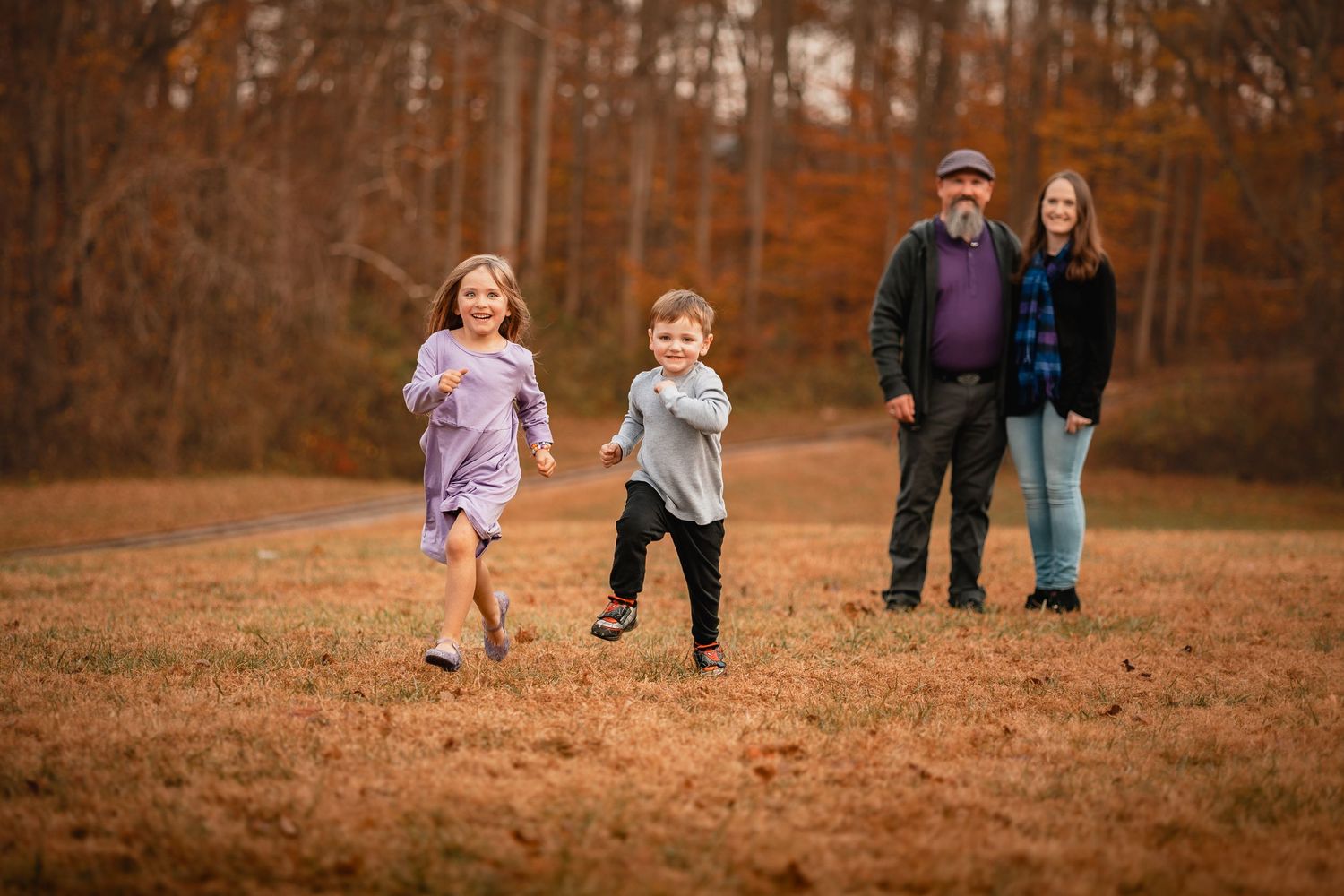 Children run and play together across a rustic autumn field covered in fallen leaves during golden hour.
