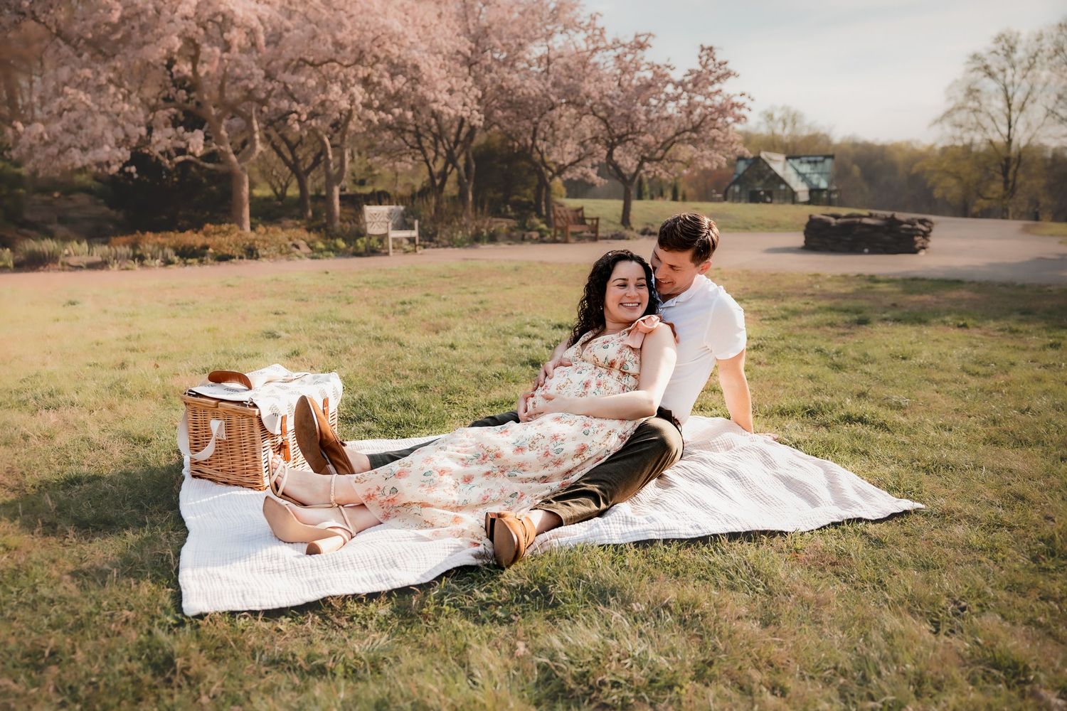 Couple enjoying a romantic spring picnic on a white blanket under blooming cherry blossom trees in a lush green park.