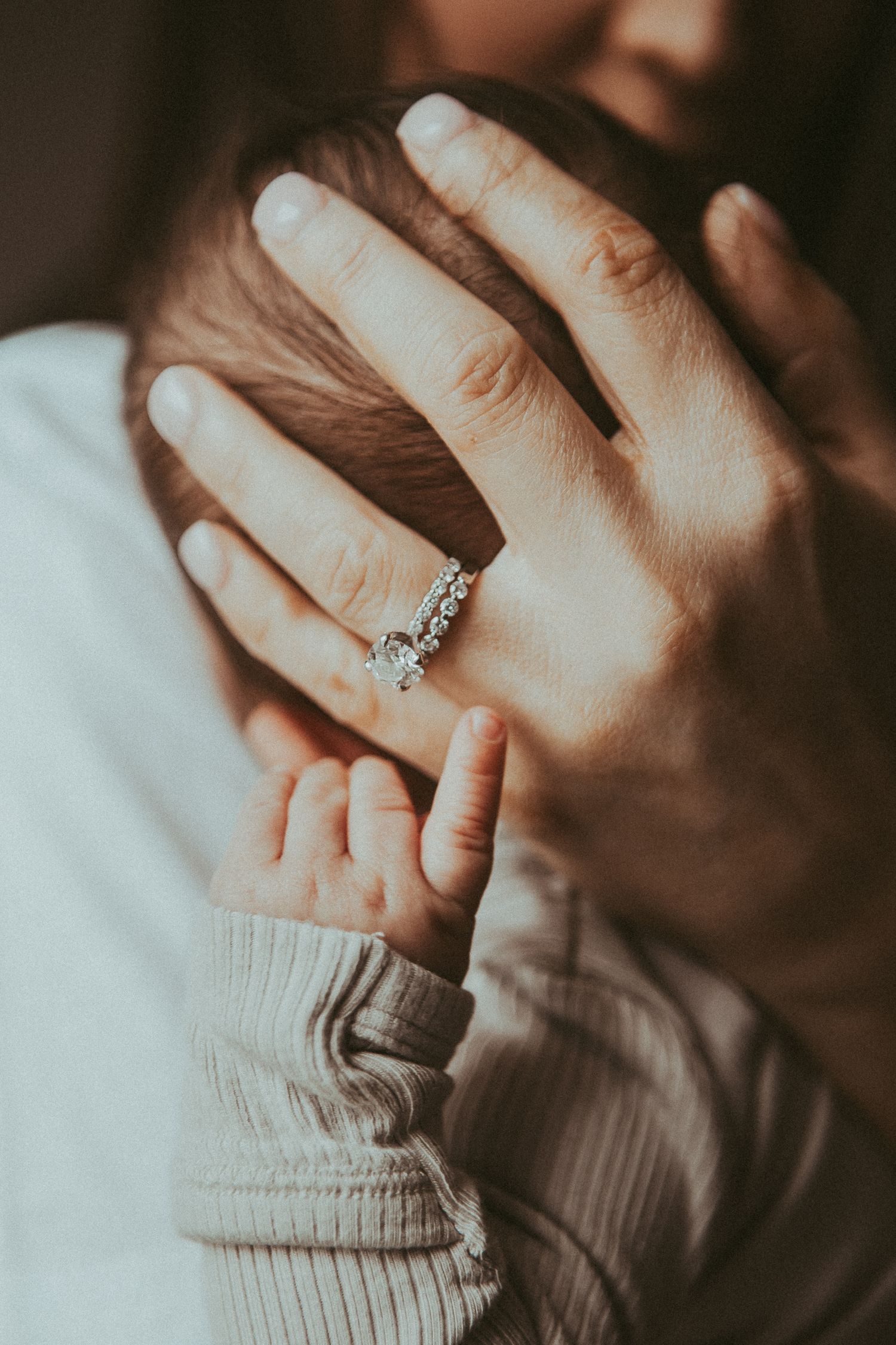 Close up view of hands wearing a diamond ring and cream sweater in moody lighting.
