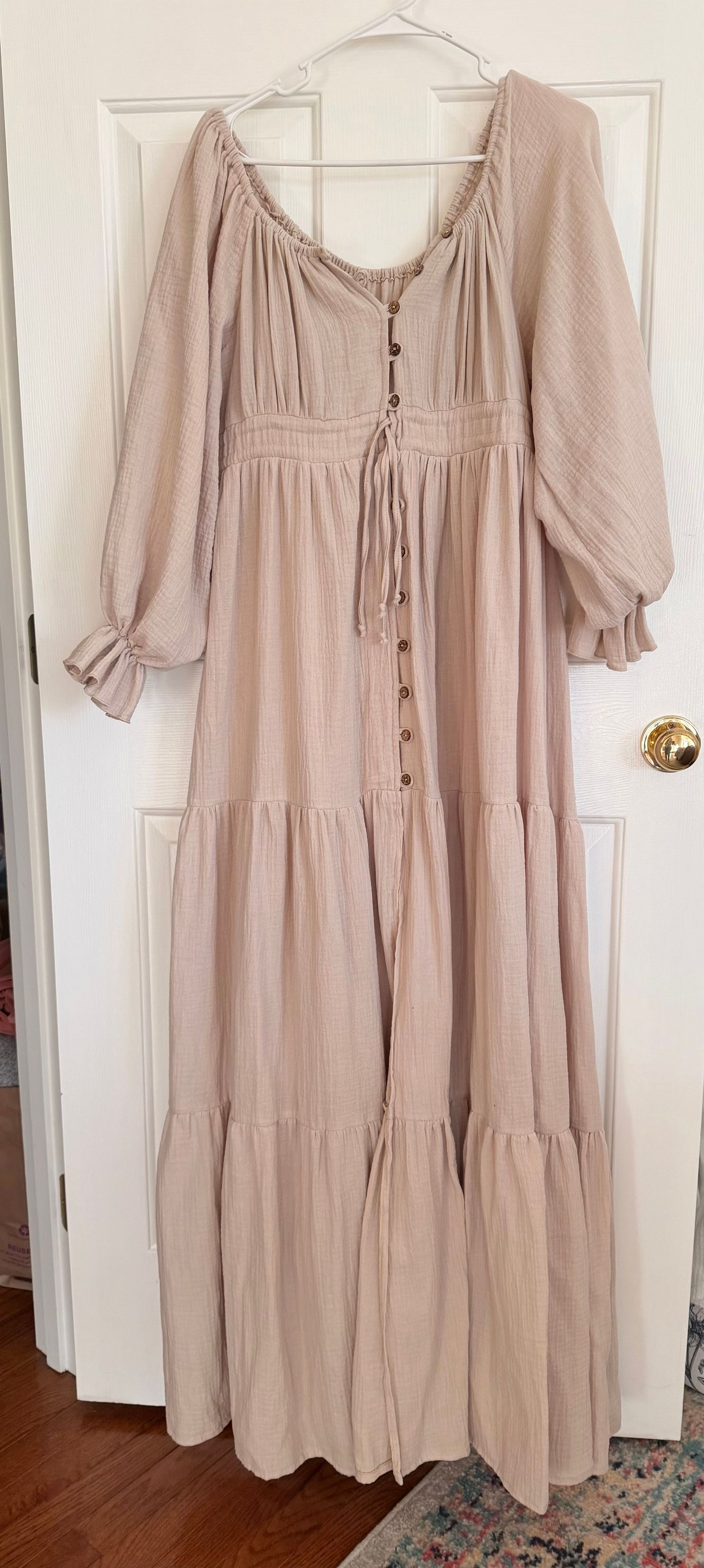 Beige tiered midi dress with puff sleeves and button front details displayed on white door in three angles.