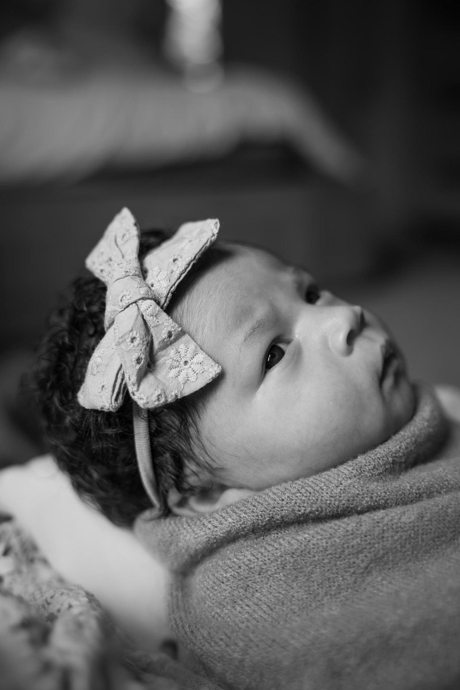 Black and white portrait of a newborn baby girl wearing a decorative bow headband, wrapped in a soft blanket.