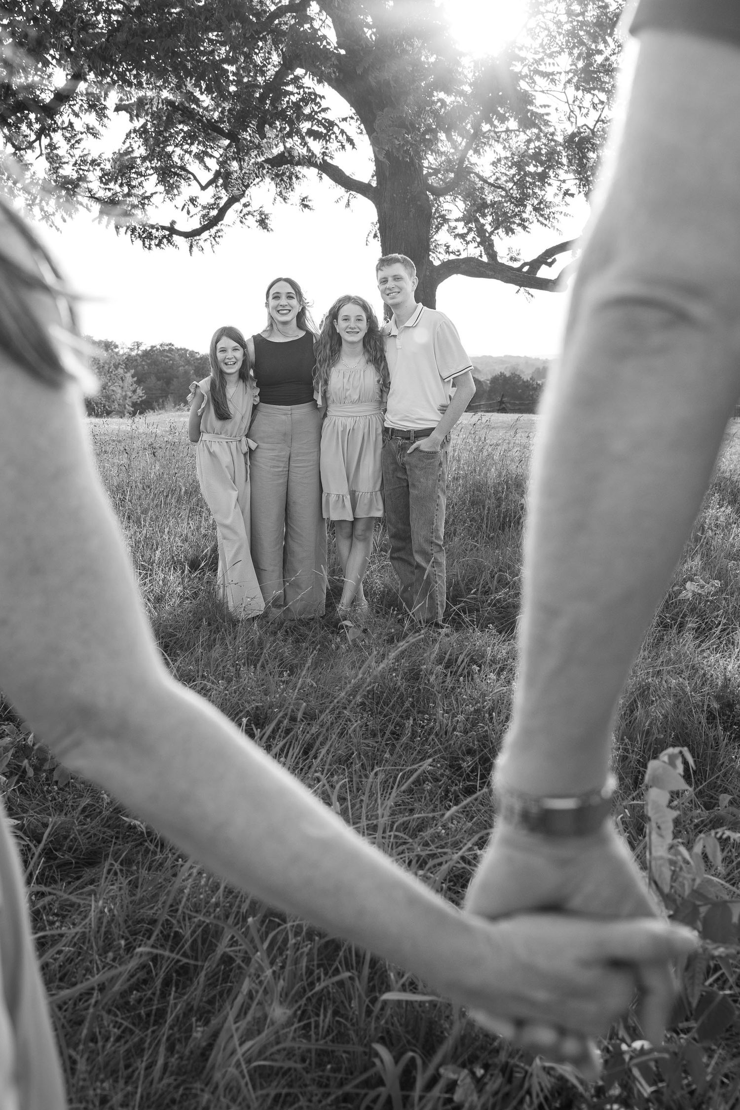 A black and white photo of parents holding hands as four children stand together under a tree.